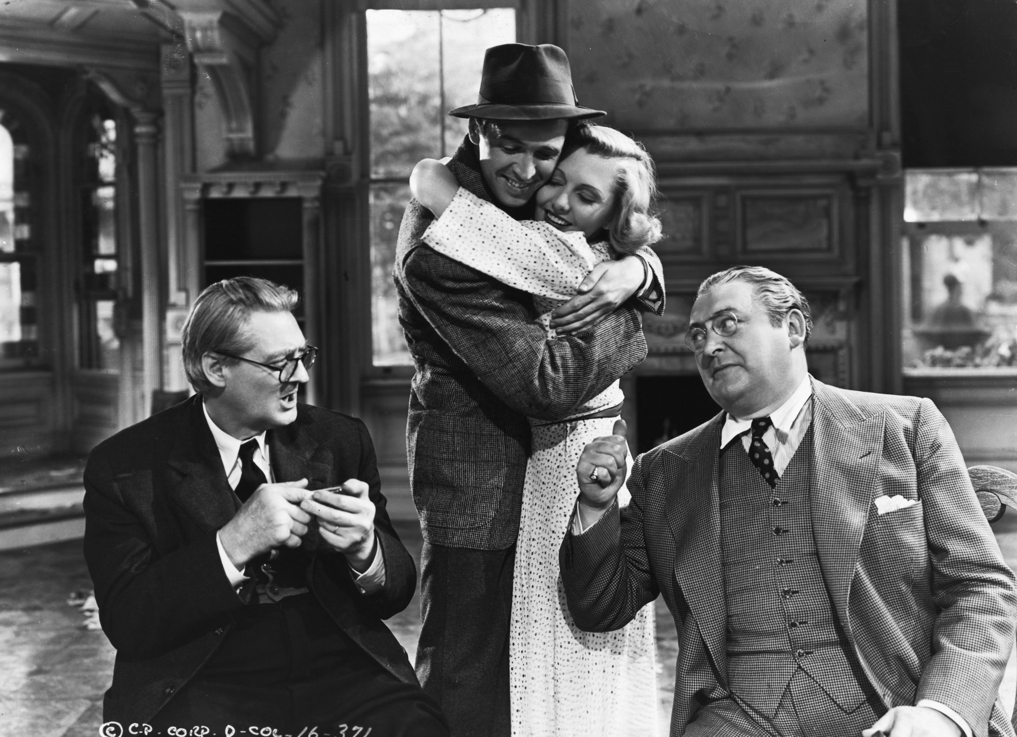 'You Can't Take It With You' Lionel Barrymore as Martin Vanderhof, Jimmy Stewart as Tony Kirby, Jean Arthur as Alice Sycamore, and Edward Arnold as Anthony Kirby sitting around a table with Stewart and Arthur hugging each other