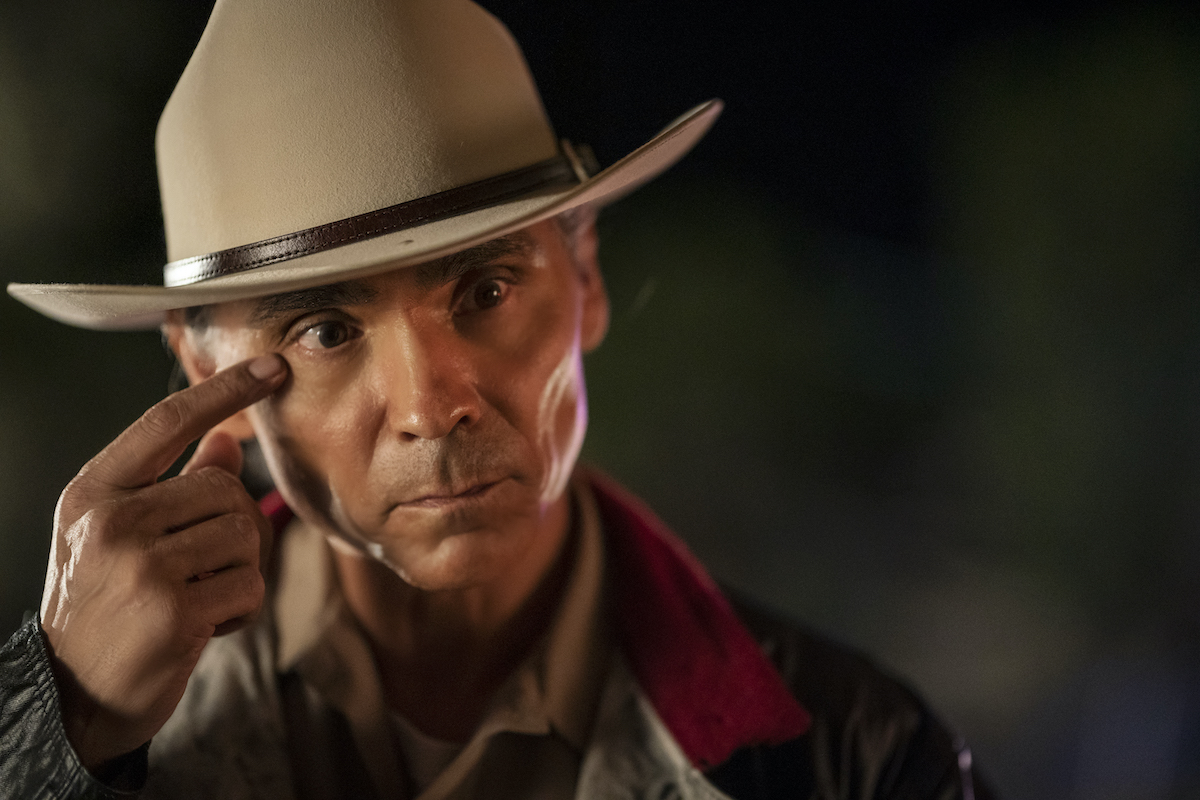 Zahn McClarnon wearing a hat and touching his finger to his face in 'Dark Winds'