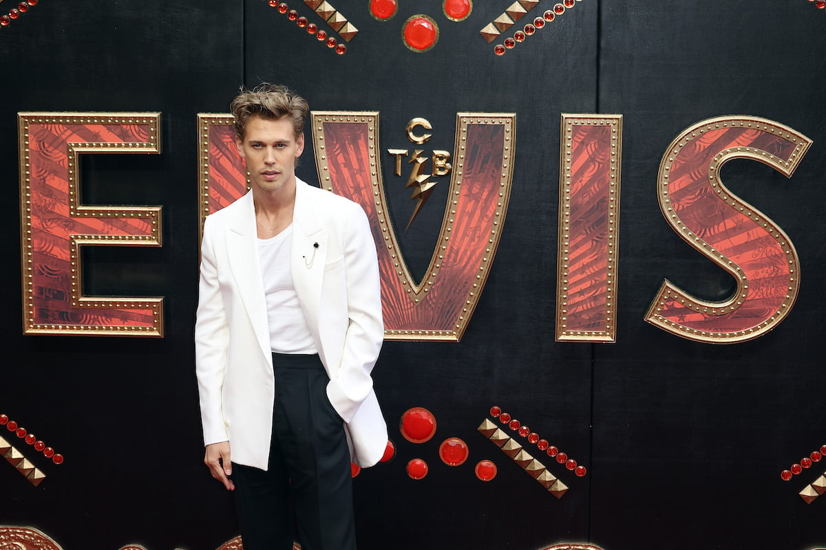 Austin Butler posing in a white jacket in front of an 'Elvis' backdrop