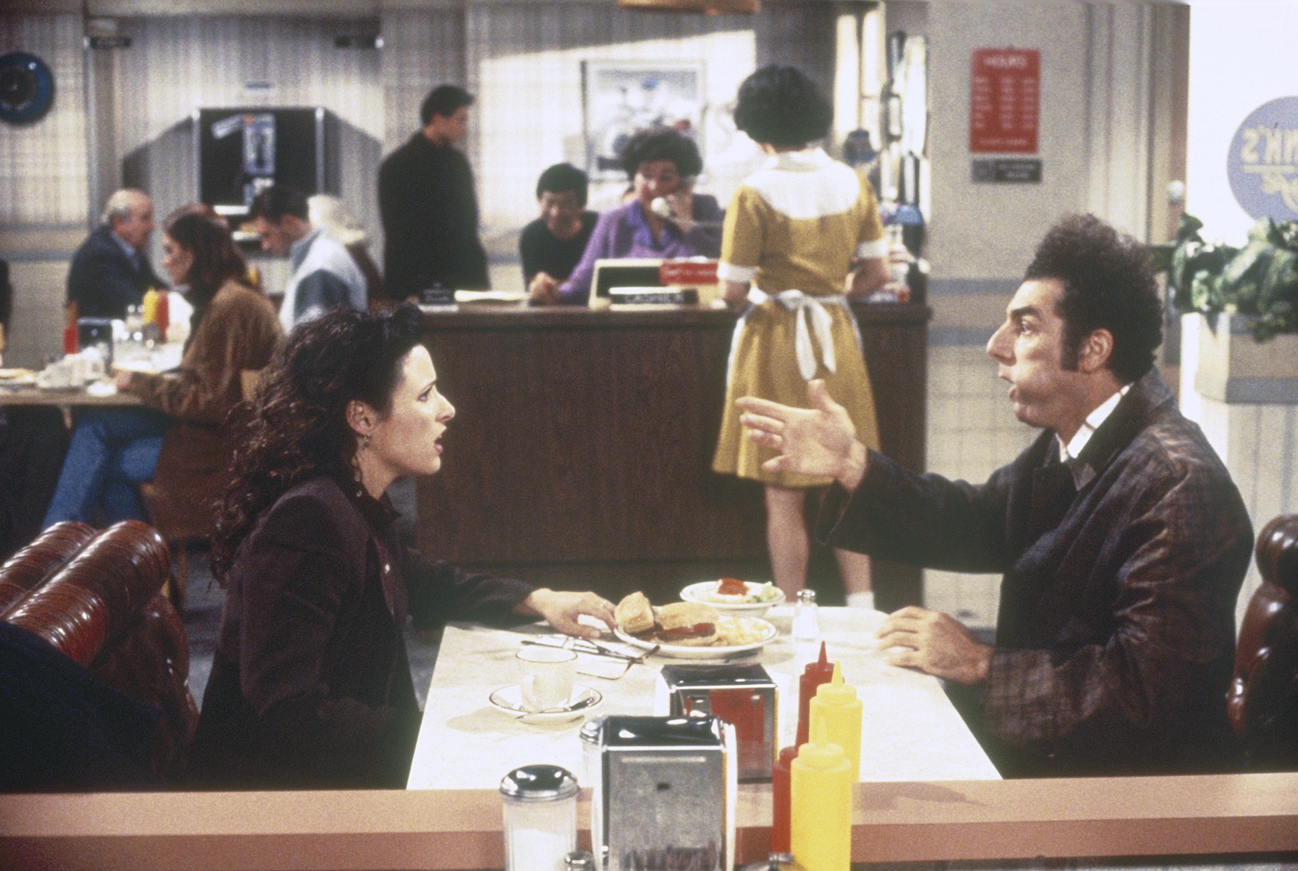 Julia Louis-Dreyfus as Elaine Benes and Michael Richards as Cosmo Kramer sit in Monk's