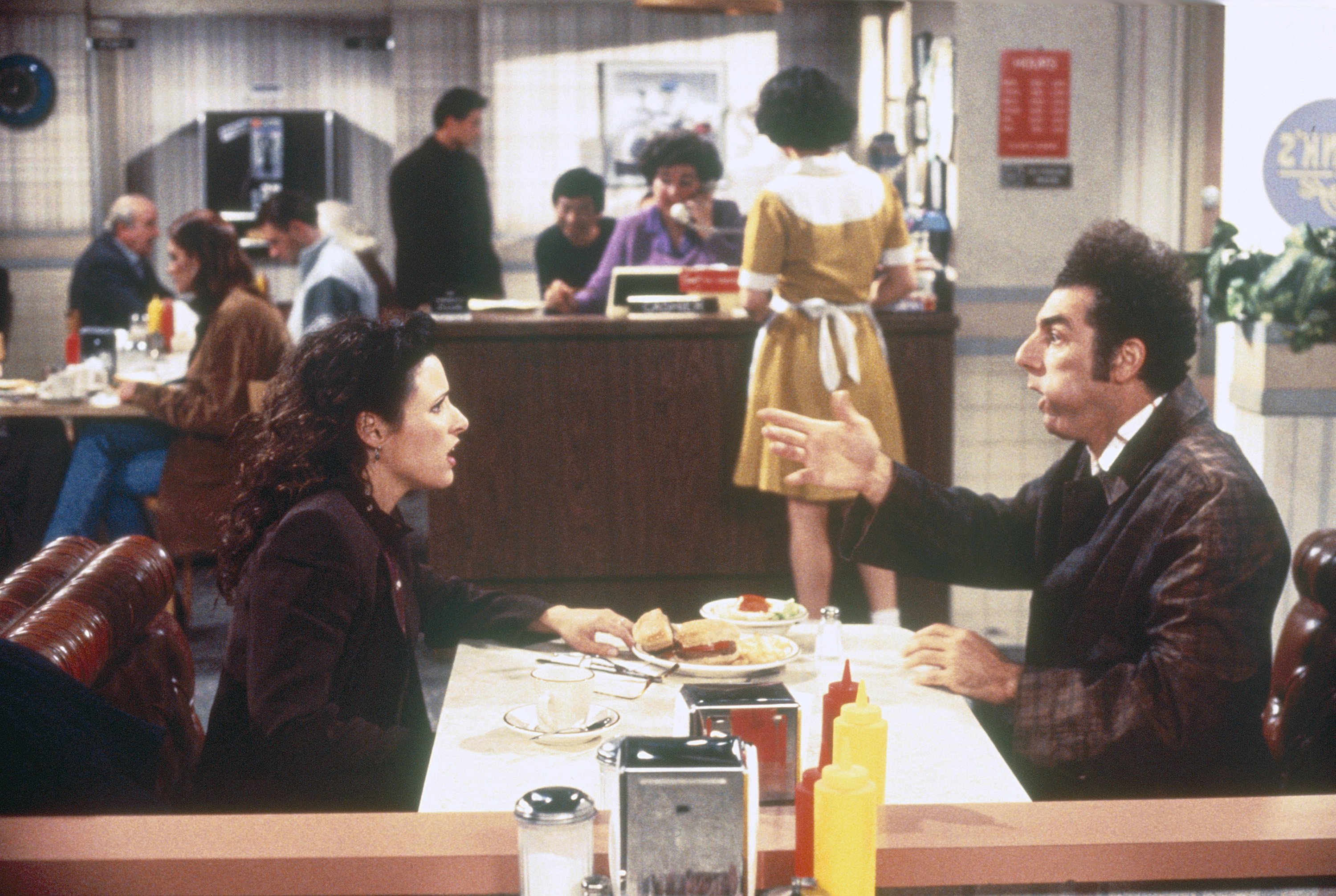 Julia Louis-Dreyfus as Elaine Benes and Michael Richards as Cosmo Kramer sit in Monk's 