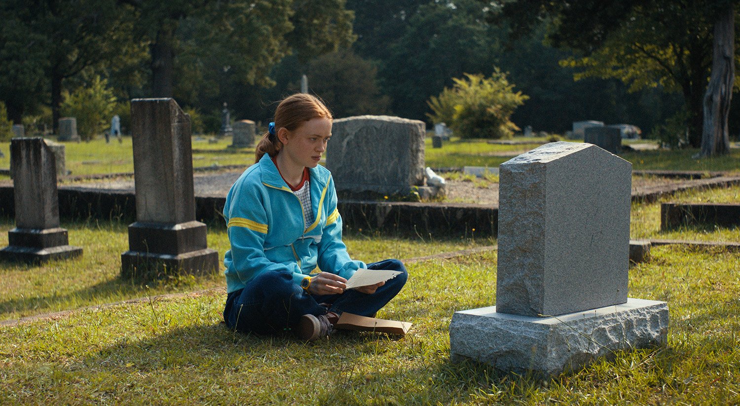 Sadie Sink as Max Mayfield sitting in a graveyard in Stranger Things 4