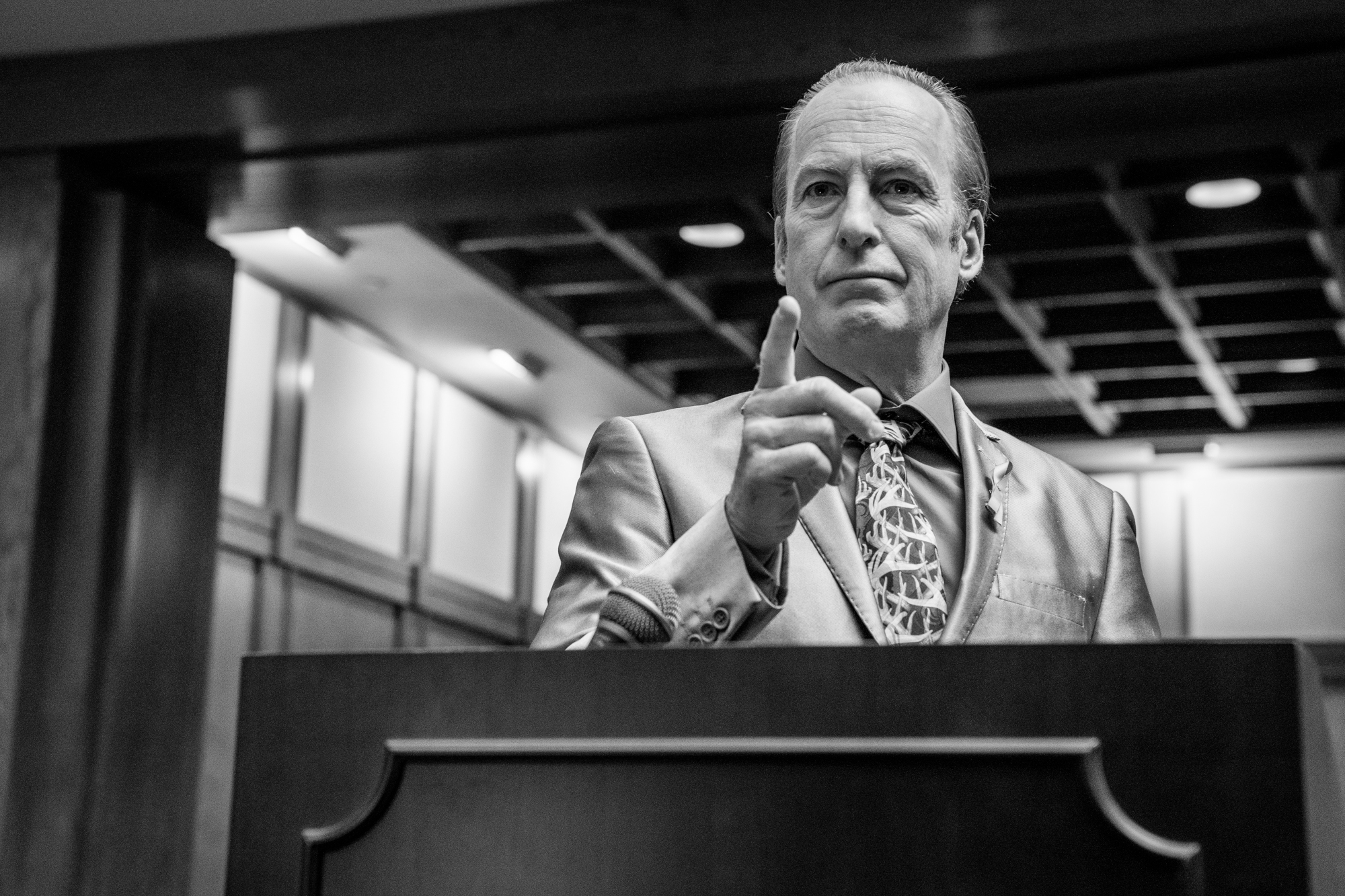 Bob Odenkirk at the ending of 'Better Call Saul' Season 6. He's standing at a podium in a courtroom and pointing forward.