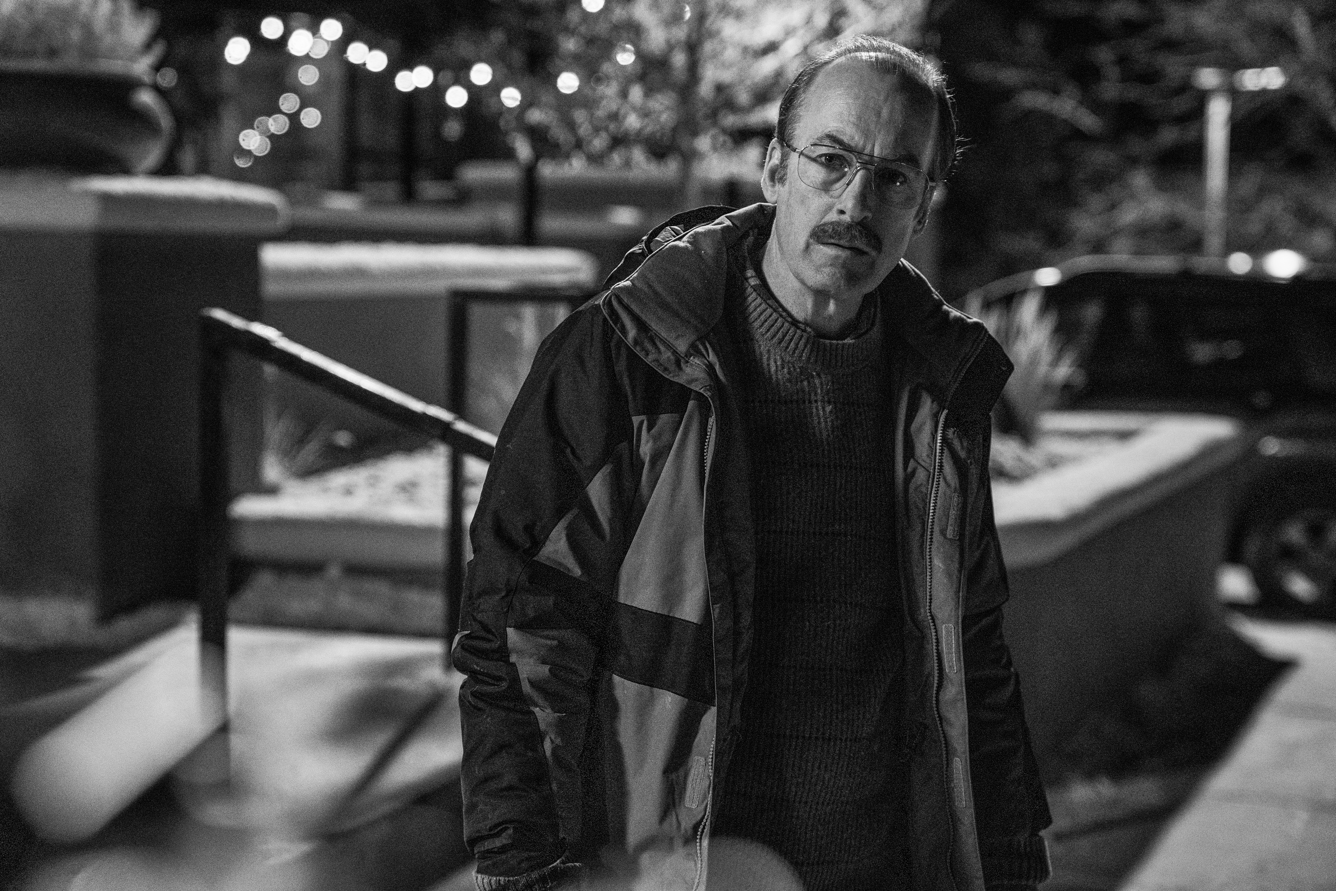 Bob Odenkirk as Gene Takovic in 'Better Call Saul' Season 6 Episode 11 on AMC. The image is in black and white, he's wearing a jacket, and he's tilting his head at someone off-screen.
