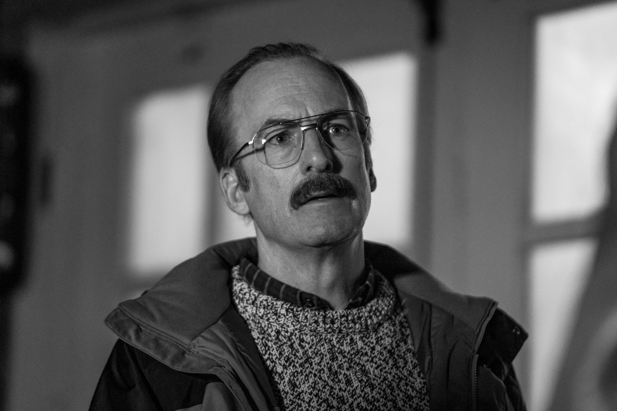 Bob Odenkirk as Gene Takovic in 'Better Call Saul' Season 6 Episode 11 for our article about the episode 12 teaser. The image is in black and white, and Gene is wearing a sweater, jacket, and glasses.