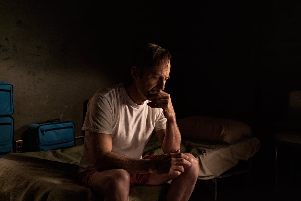 Bob Odenkirk as Saul Goodman in the Better Call Saul series finale. Saul sits on a bed and looks serious. 