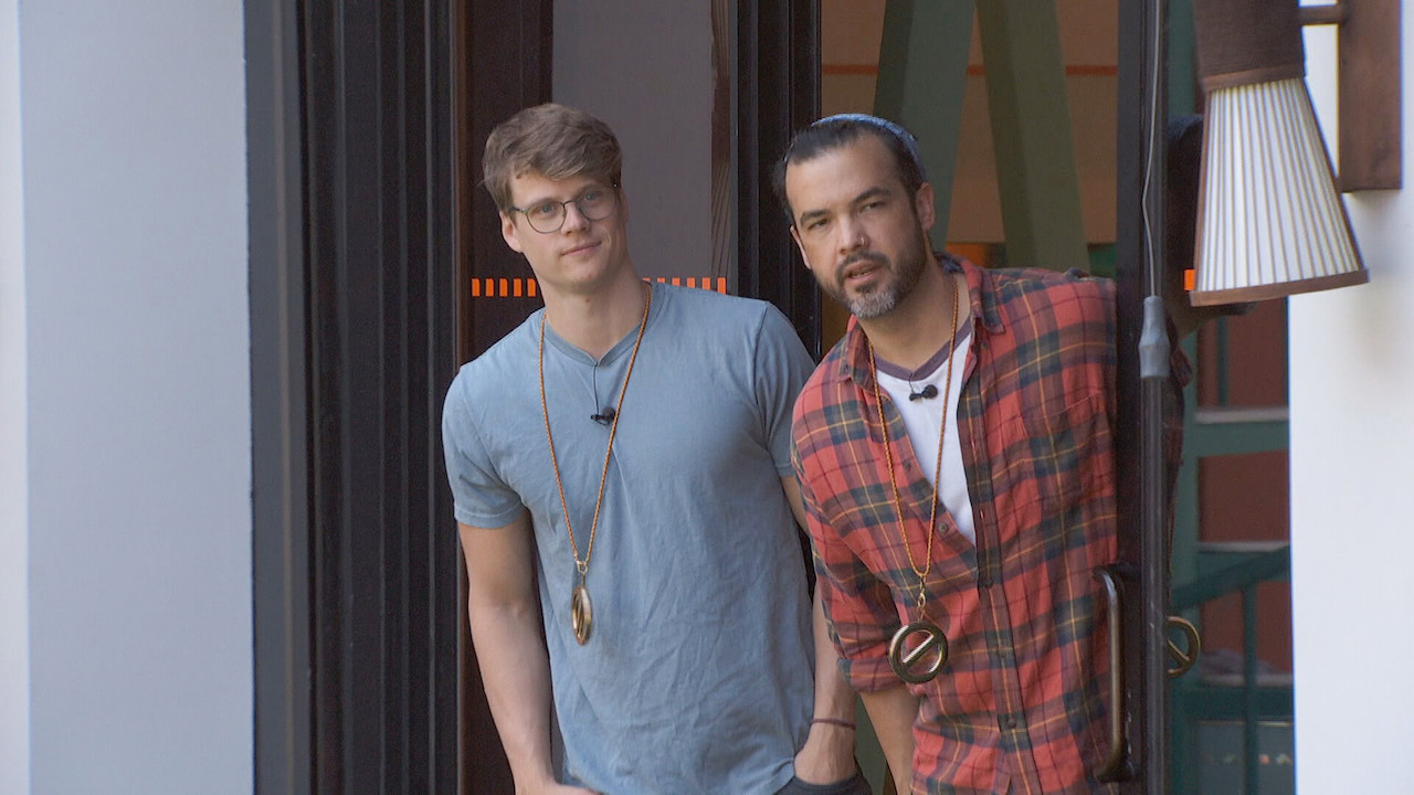 Kyle and Daniel wear power of veto necklaces as they lean out a door into the backyard.