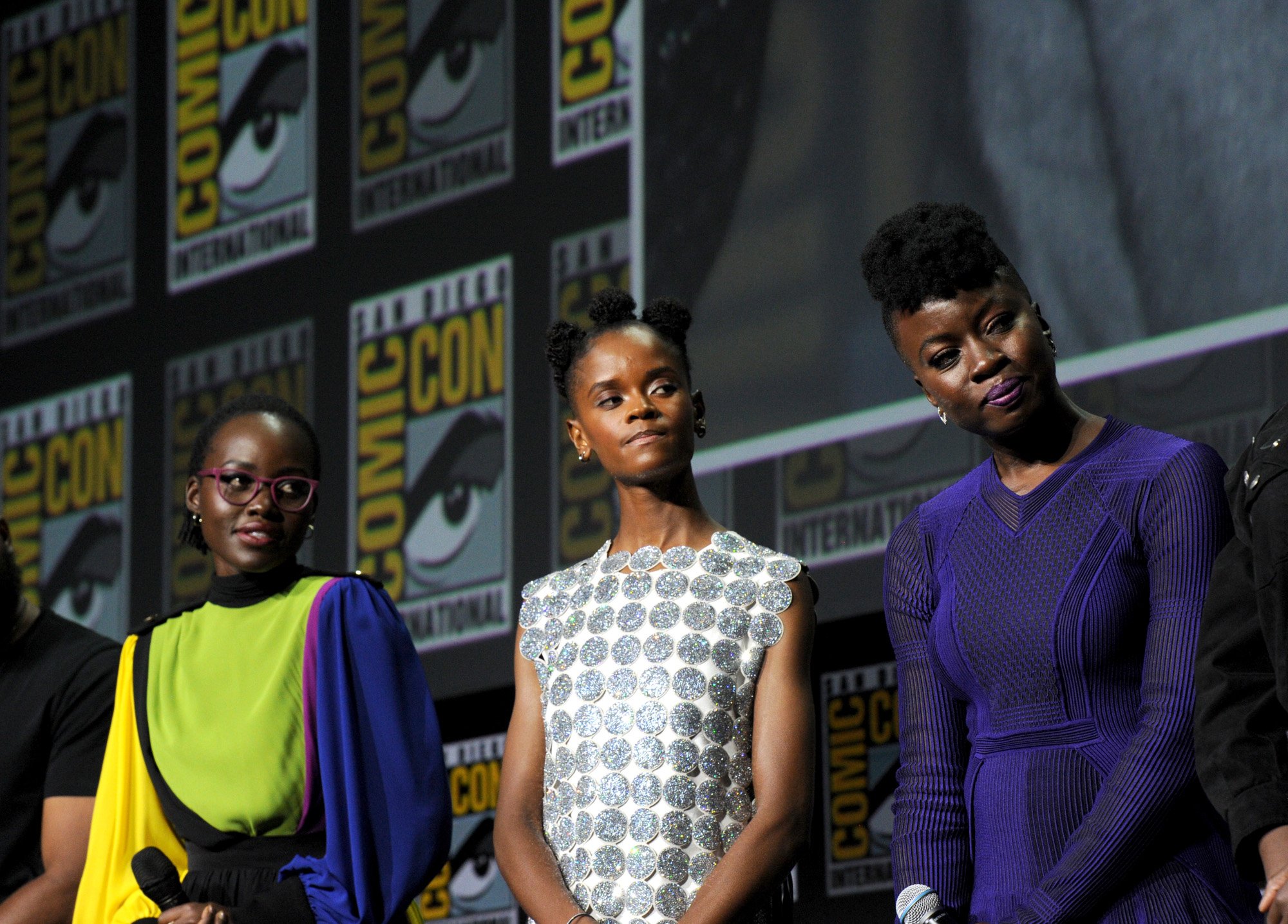 Lupita Nyong'o, Letitia Wright, and Danai Gurira during the 'Black Panther: Wakanda Forever' panel at San Diego Comic-Con, which also debuted the first trailer. The three are standing next to one another, and they're looking at something to the left of the camera.