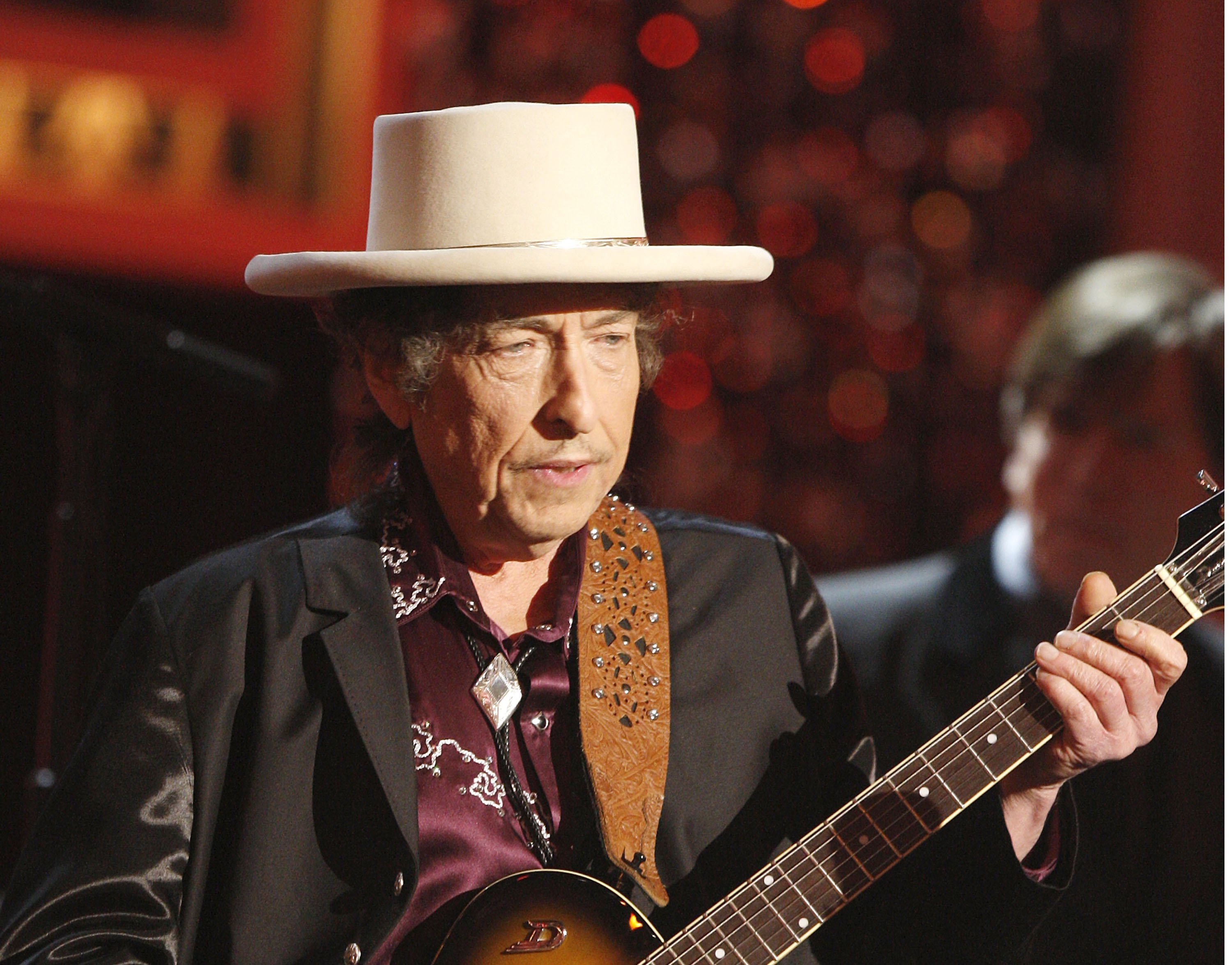 Bob Dylan wears a hat and holds a guitar.