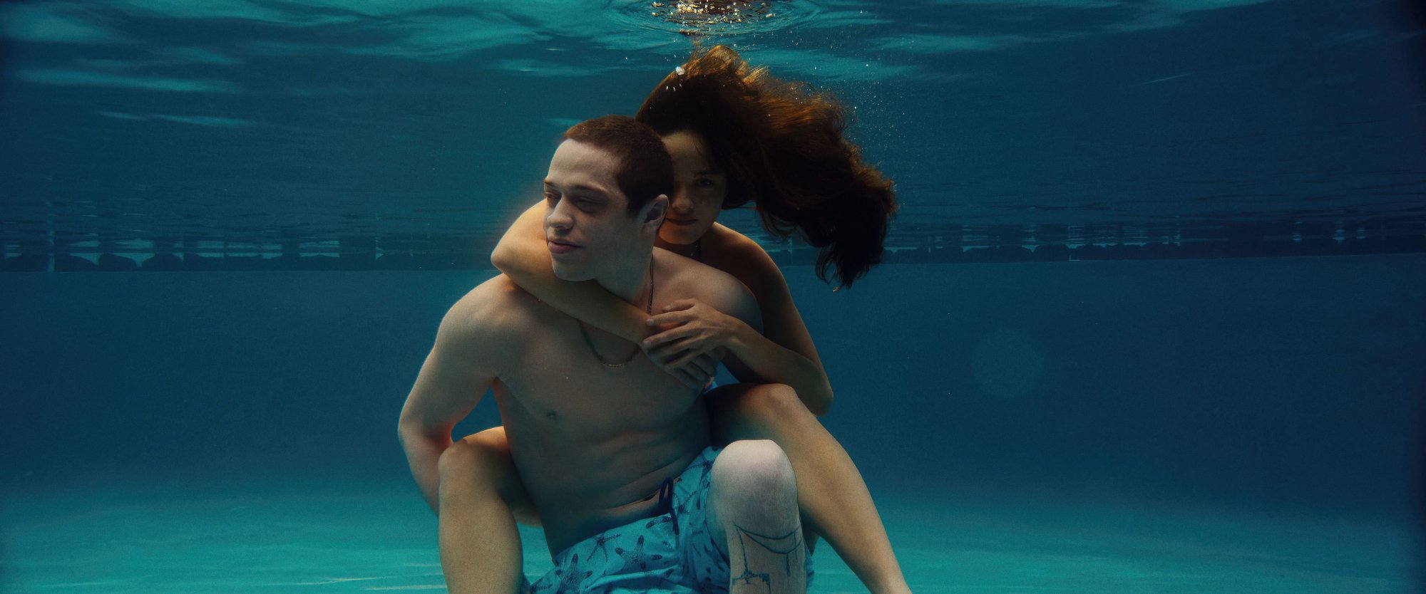 'Bodies Bodies Bodies' Pete Davidson as David and Chase Sui Wonders as Emma. They're underwater wearing bathing suits with her hanging onto him on his back.