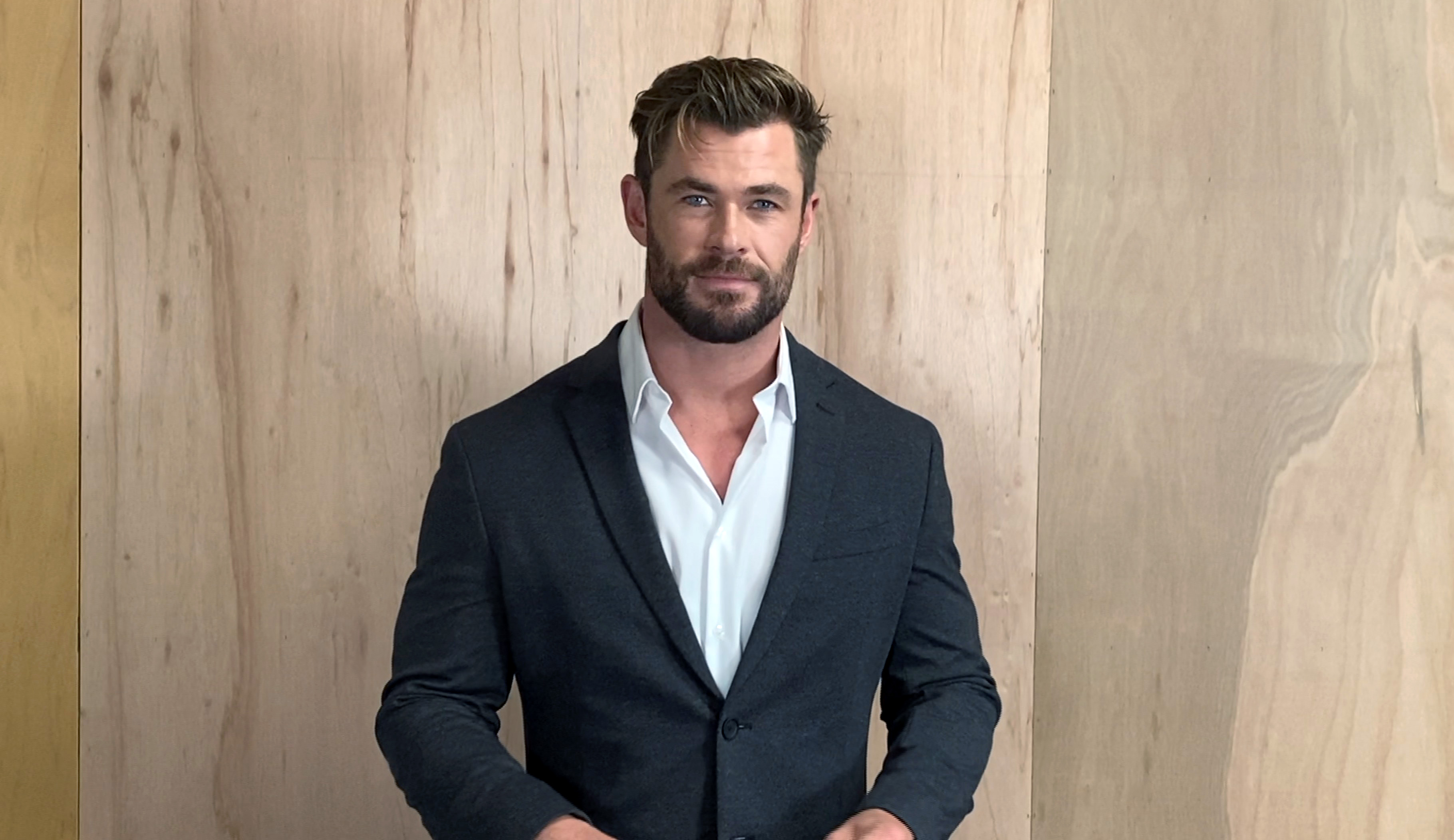 Chris Hemsworth smiles while posing in a shirt and suit jacket.