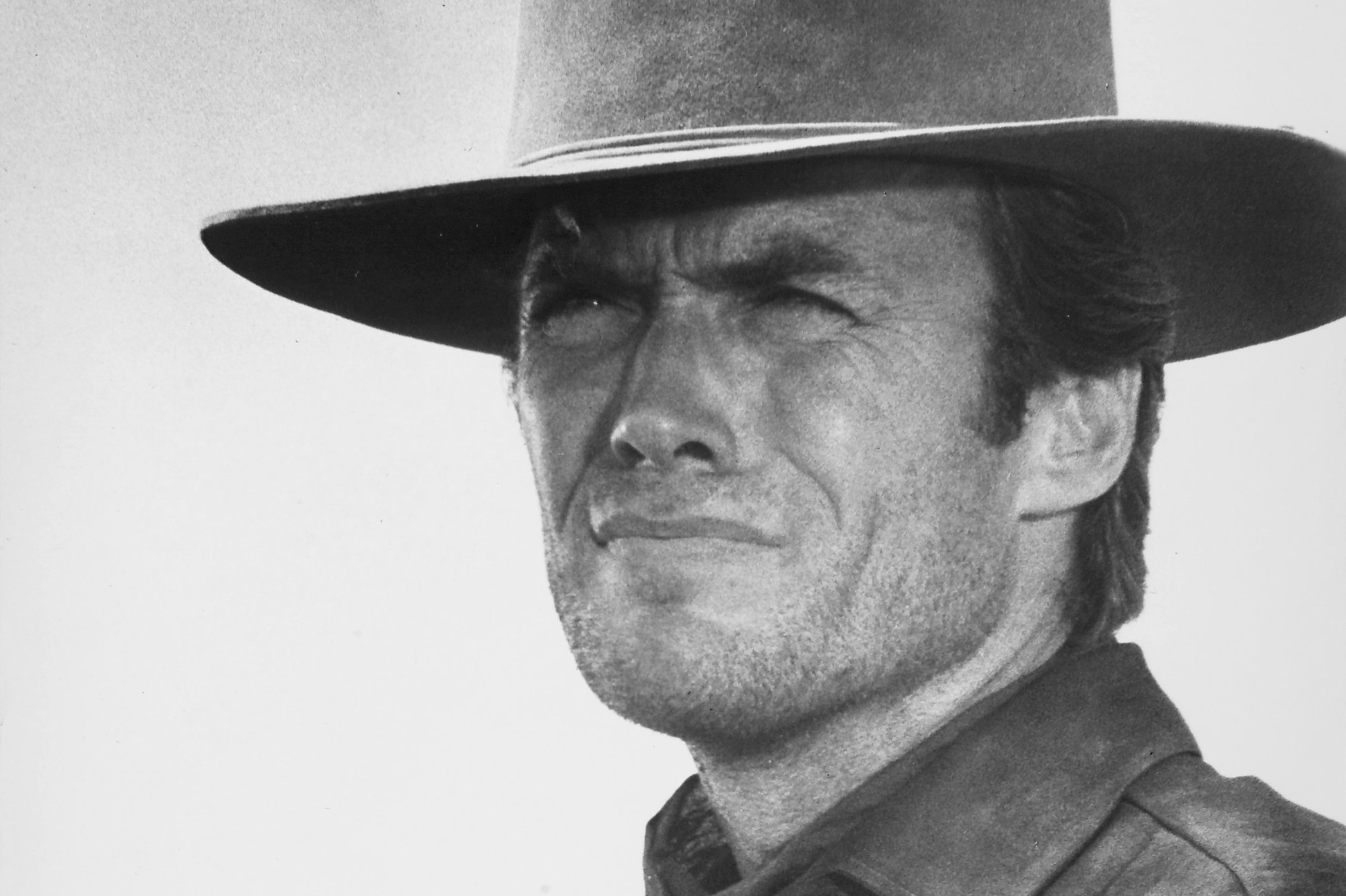 Clint Eastwood as Marshal Jed Cooper in the movie 'Hang 'Em High.' The black-and-white picture shows Eastwood squinting wearing a cowboy hat and a collared sheriff shirt.