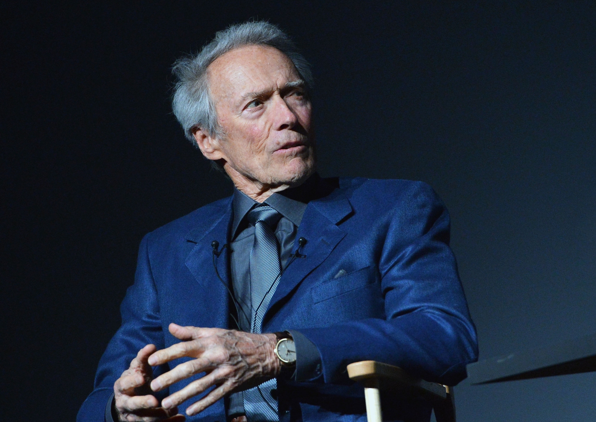 Clint Eastwood, who saved Howard Hawks' horses. He's wearing a blue suit jacket while sitting in a chair. He's looking to the side, talking.