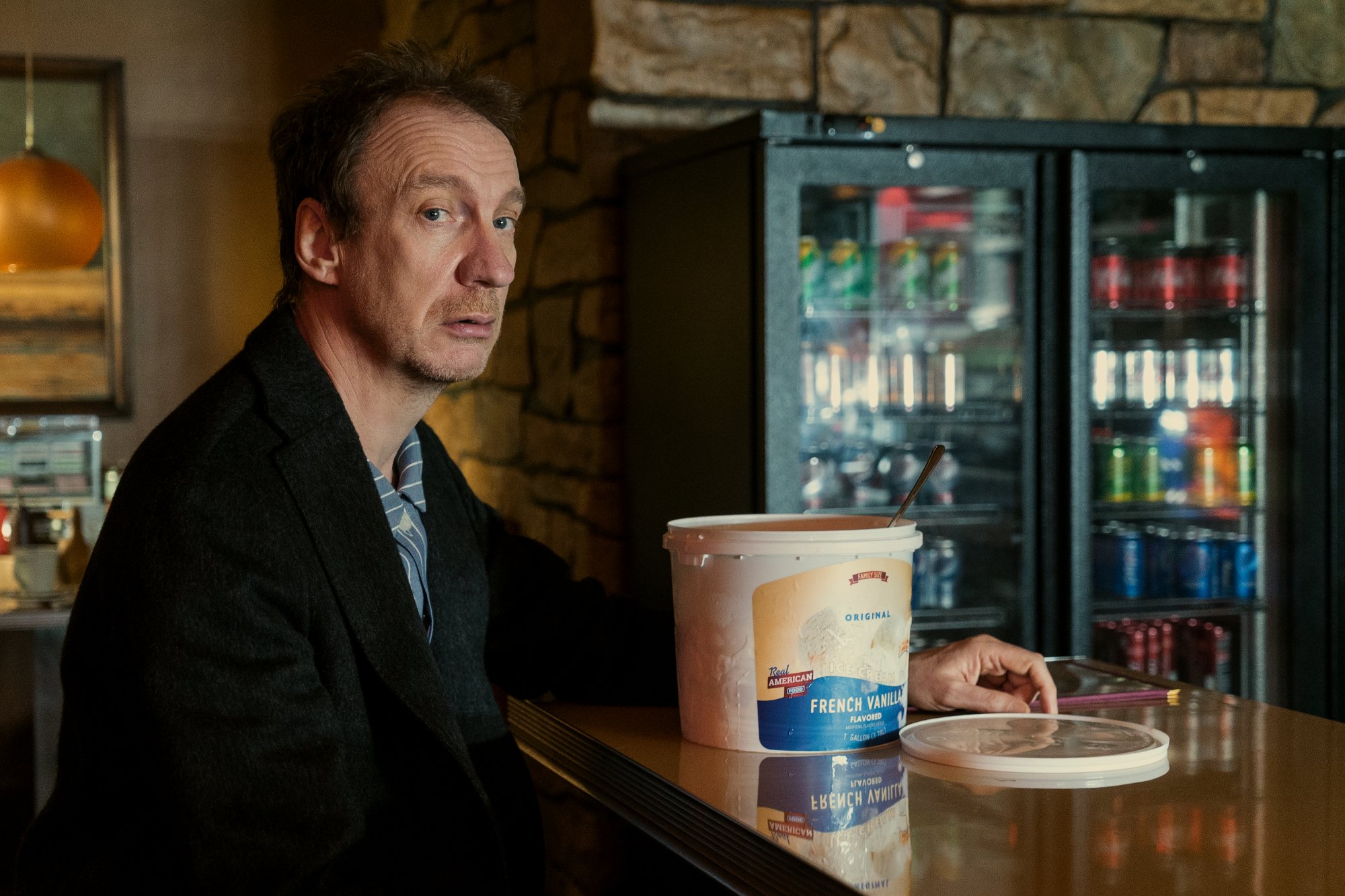 Netflixの「サンドマン」に出演する俳優のデヴィッド・シューリス。 彼はカウンターに座っていて、目の前にアイスクリームの入った桶があります。