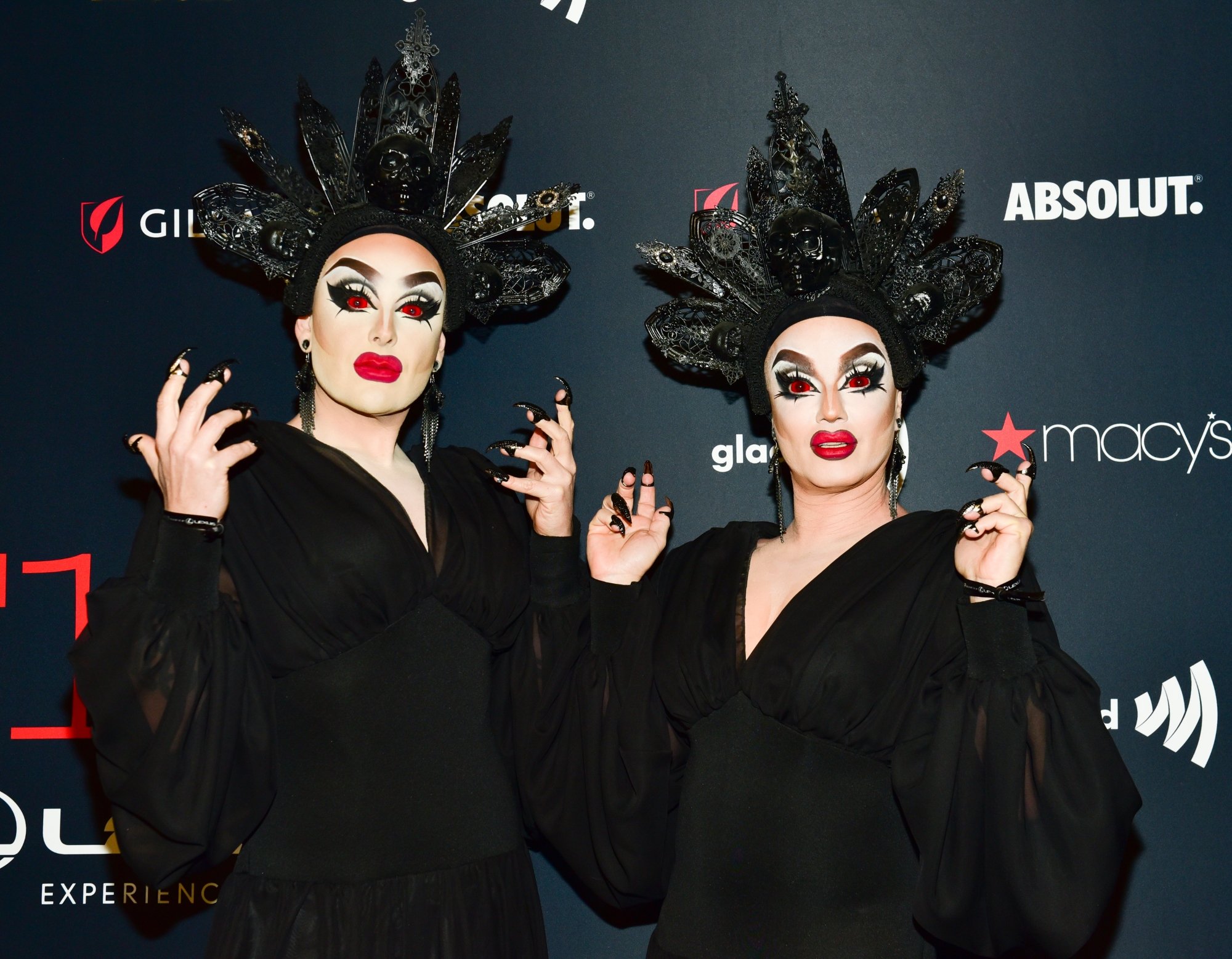 'Dragula' The Boulet Brothers wearing black dresses and head pieces in front of step and repeat