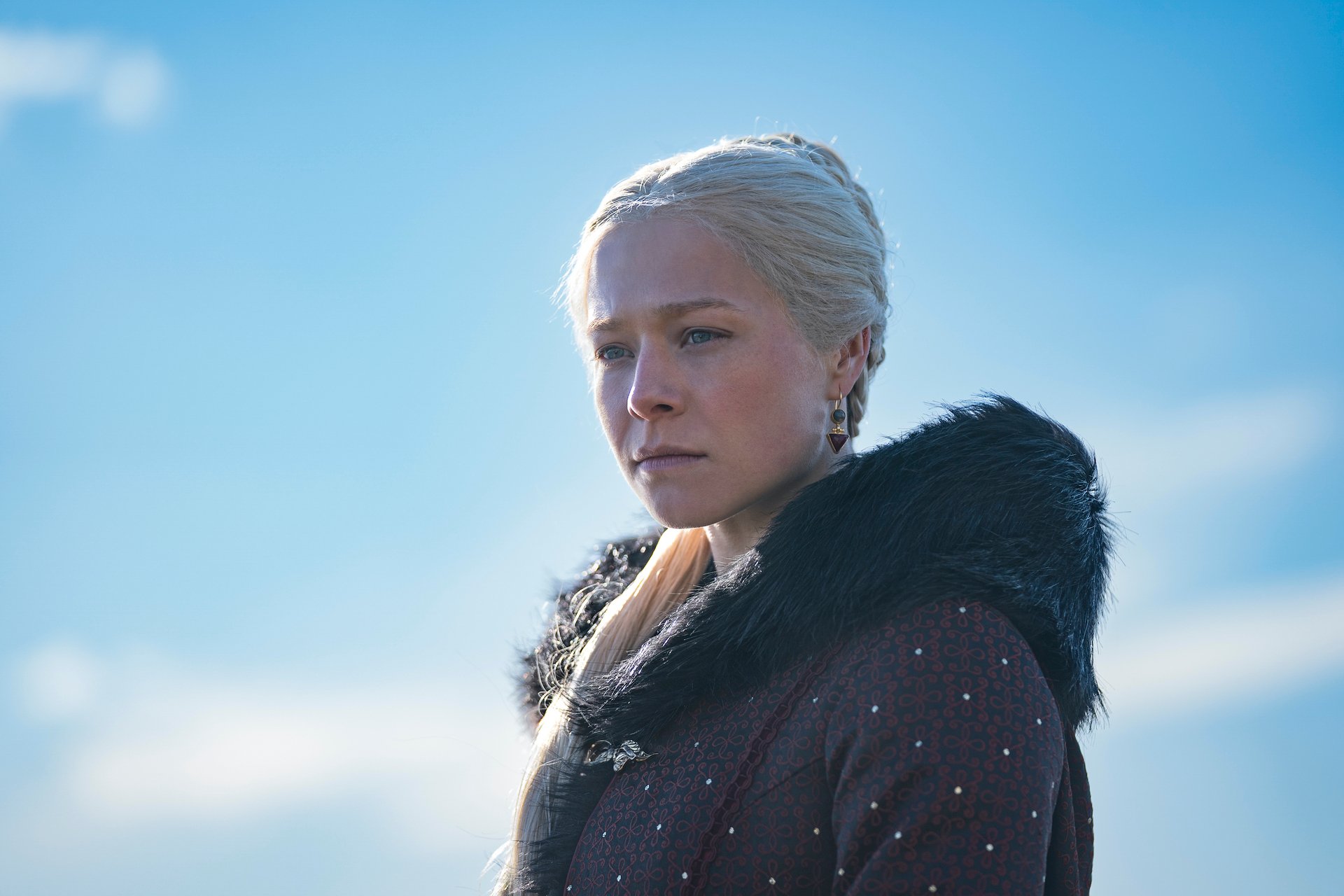 Emma D'Arcy as Princess Rhaenyra Targaryen in 'House of the Dragon' Season 1. She's wearing a black cloak and standing before a blue sky.