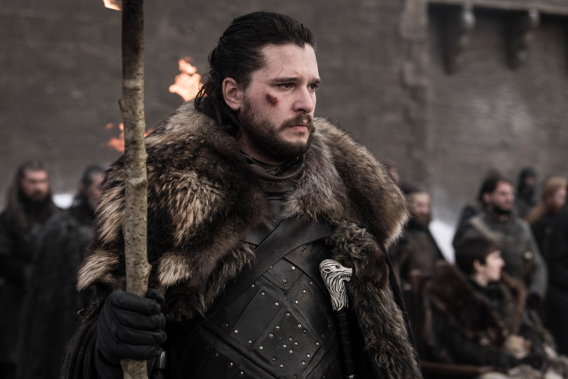 Kit Harington as Jon Snow, who will receive his own 'Game of Thrones' spinoff. In the photo, he's wearing a fur cloak and standing in front of people while holding a torch.