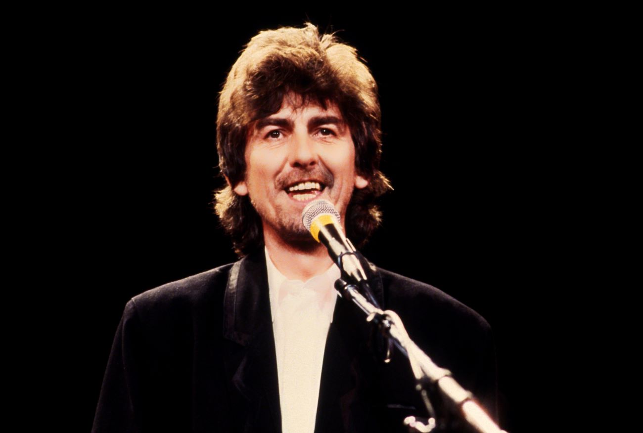 George Harrison stands in front of a microphone.