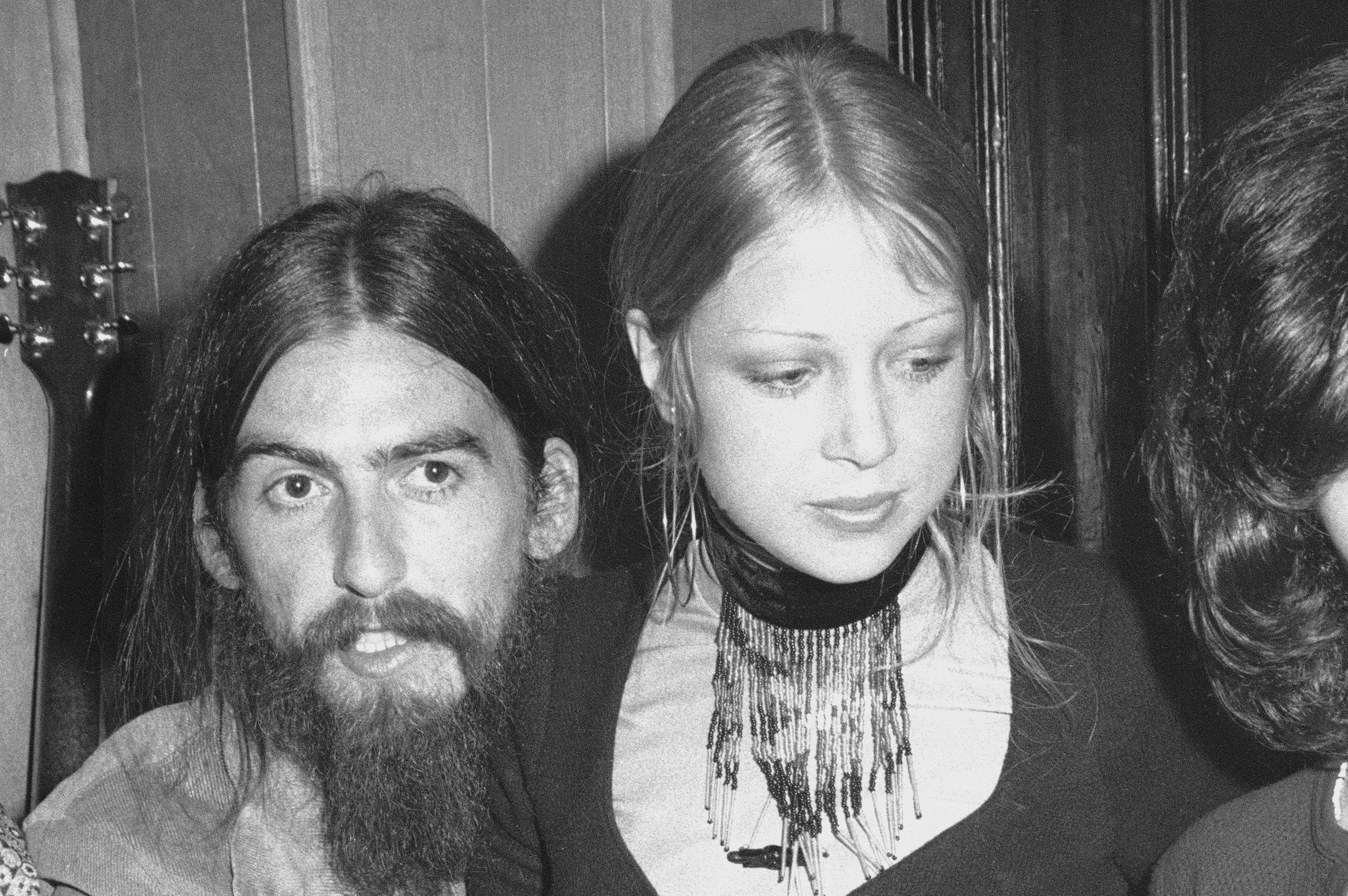 A black and white picture of George Harrison and Pattie Boyd. She sits on his lap.