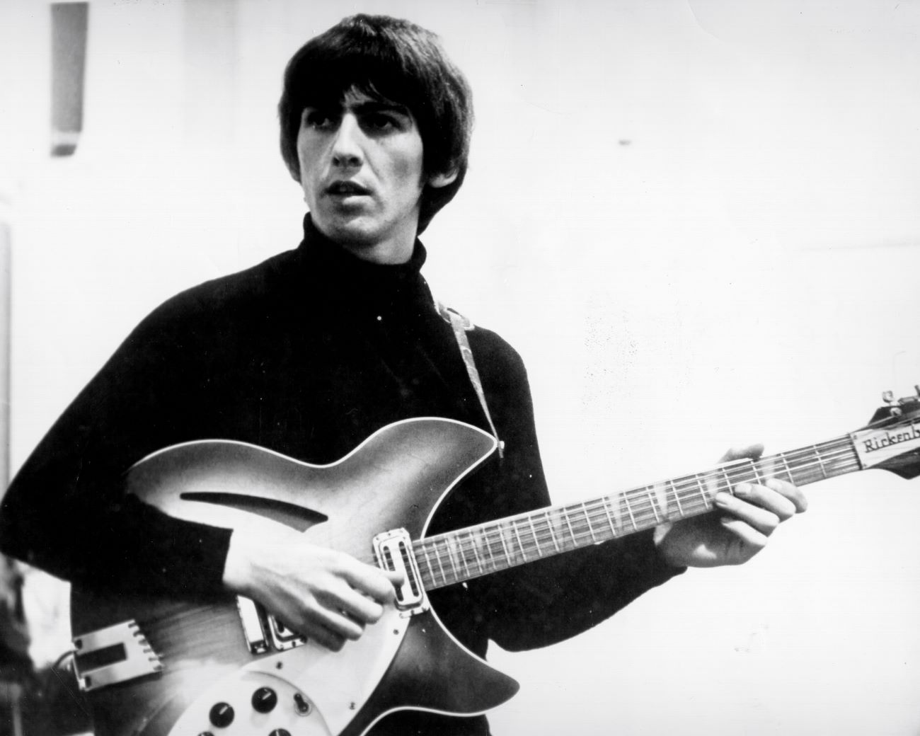 A black and white picture of The Beatles' George Harrison wearing a turtleneck and playing guitar.