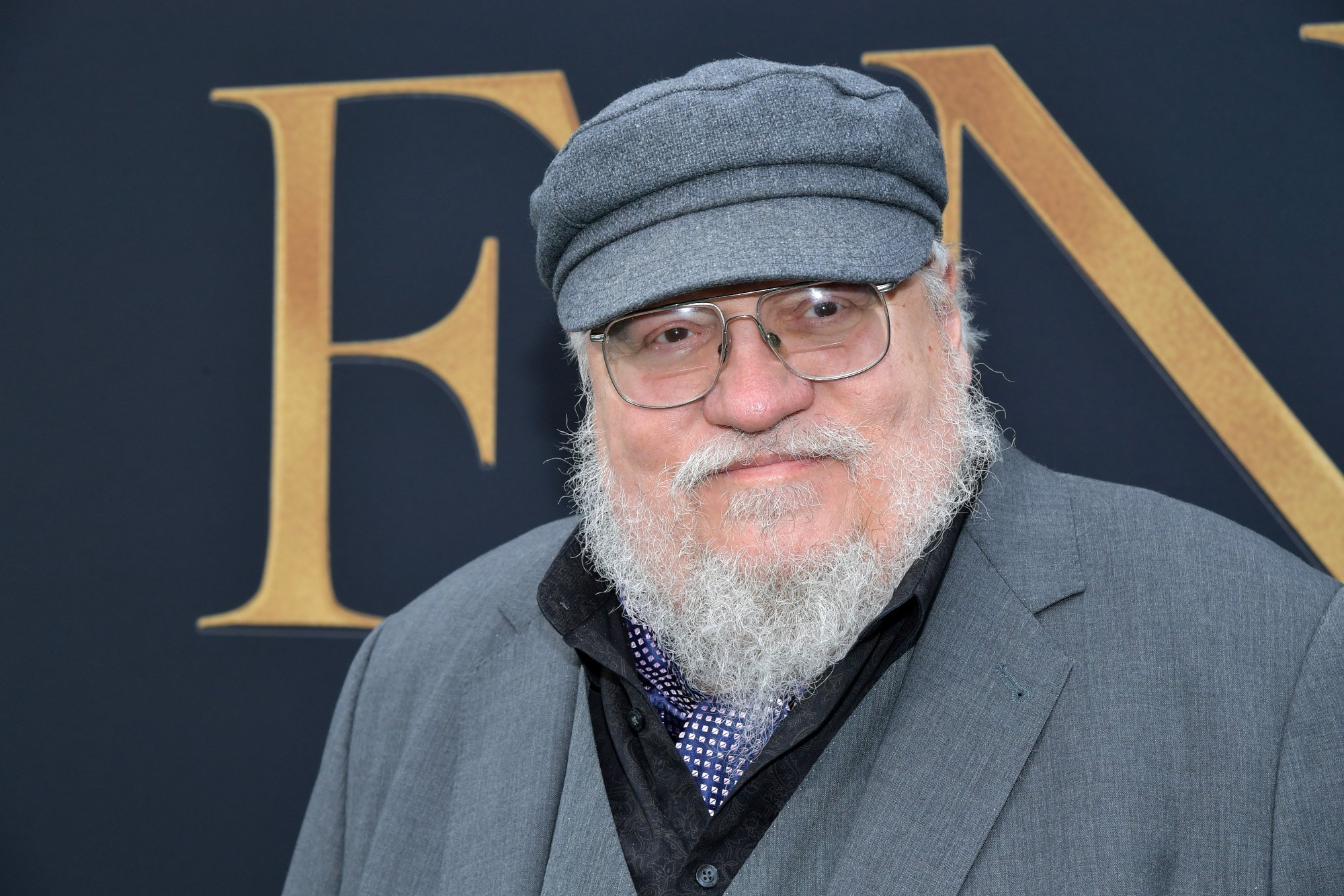 George R.R. Martin, who created the 'Game of Thrones' universe. He's wearing a grey jacket and grey hat, as well as glasses.