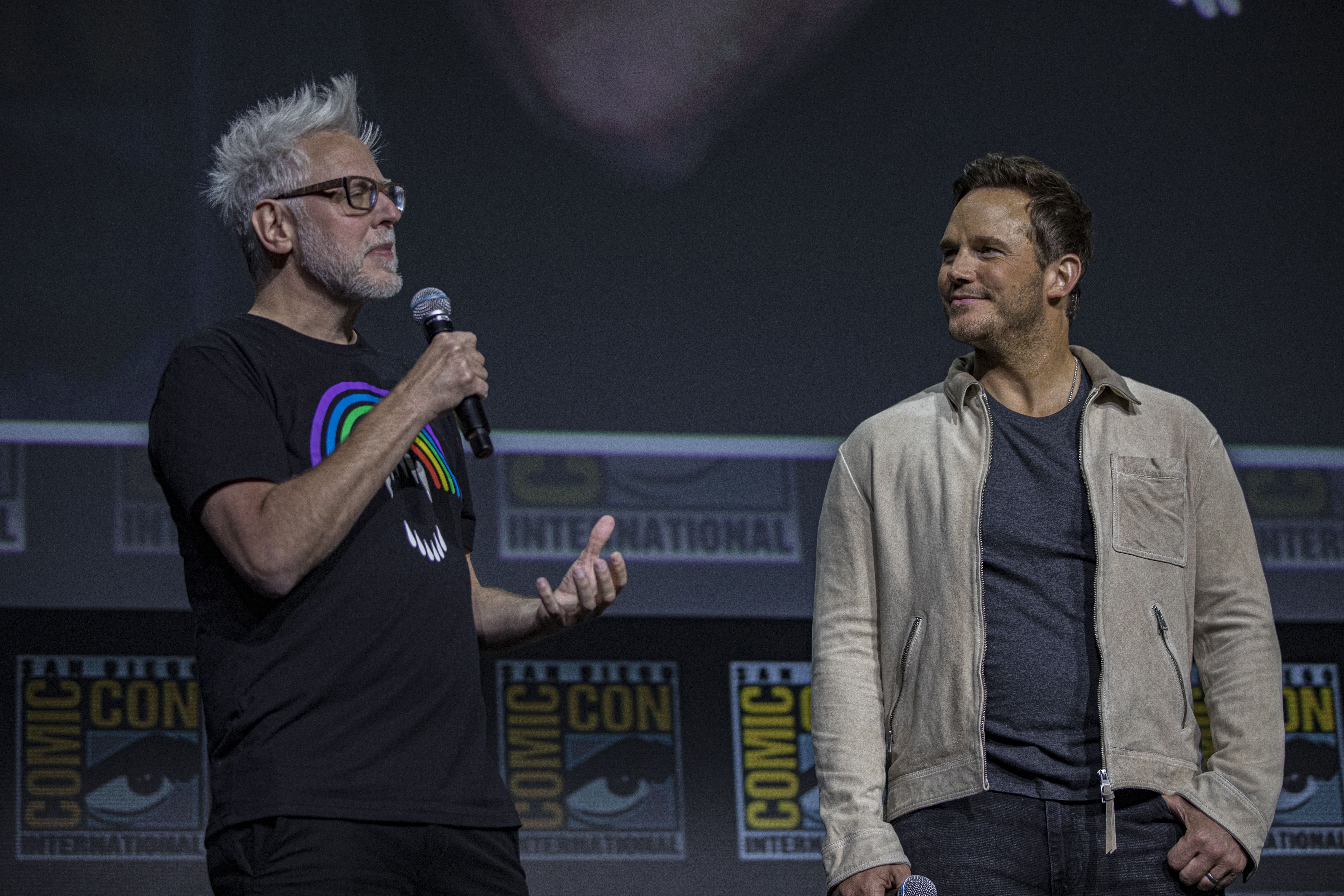 James Gunn, who teased the runtime for 'Guardians of the Galaxy 3,' speaks onstage next to Chris Pratt. Gunn wears a black shirt with a rainbow on it. Pratt wears a tan jacket over a dark blue shirt.
