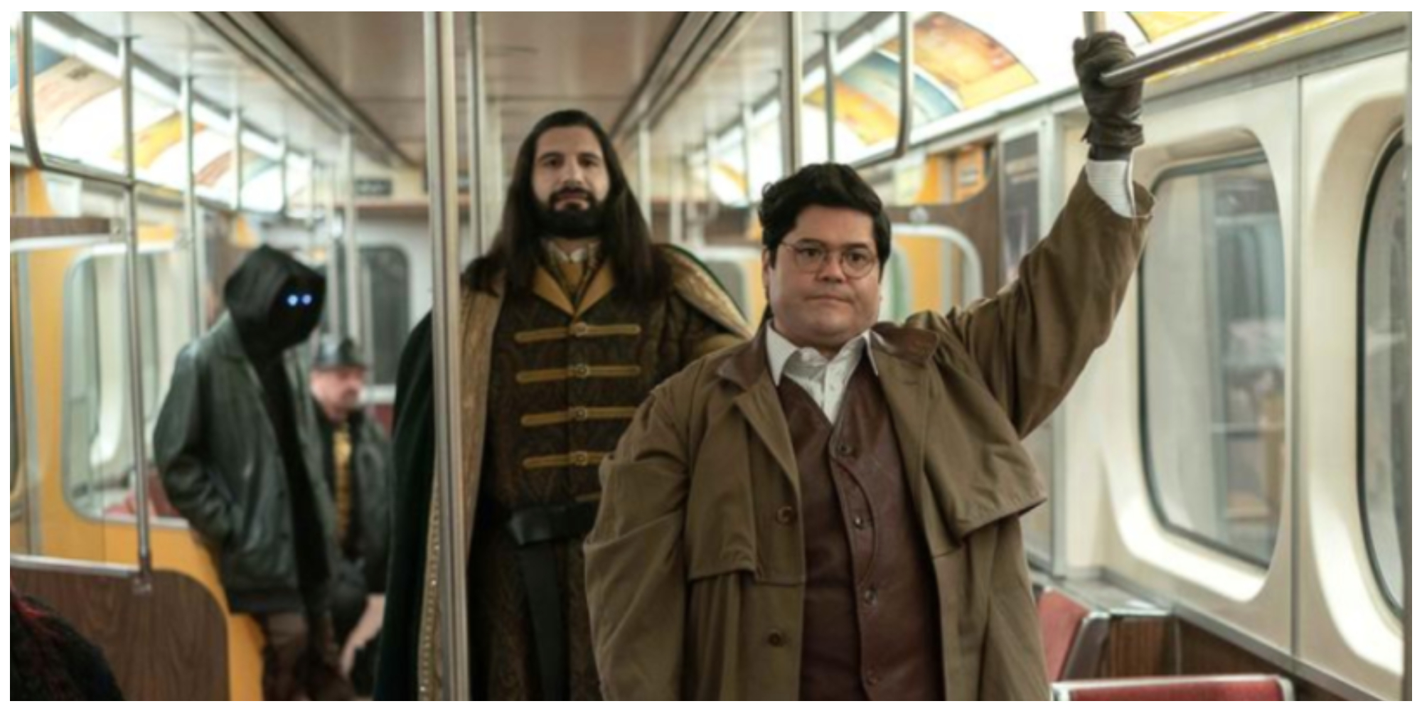 Harvey Guillén as Guillermo in 'What We Do in the Shadows' holds onto a metal bar in a subway car while Kayvan Novak as Nandor stands behind him