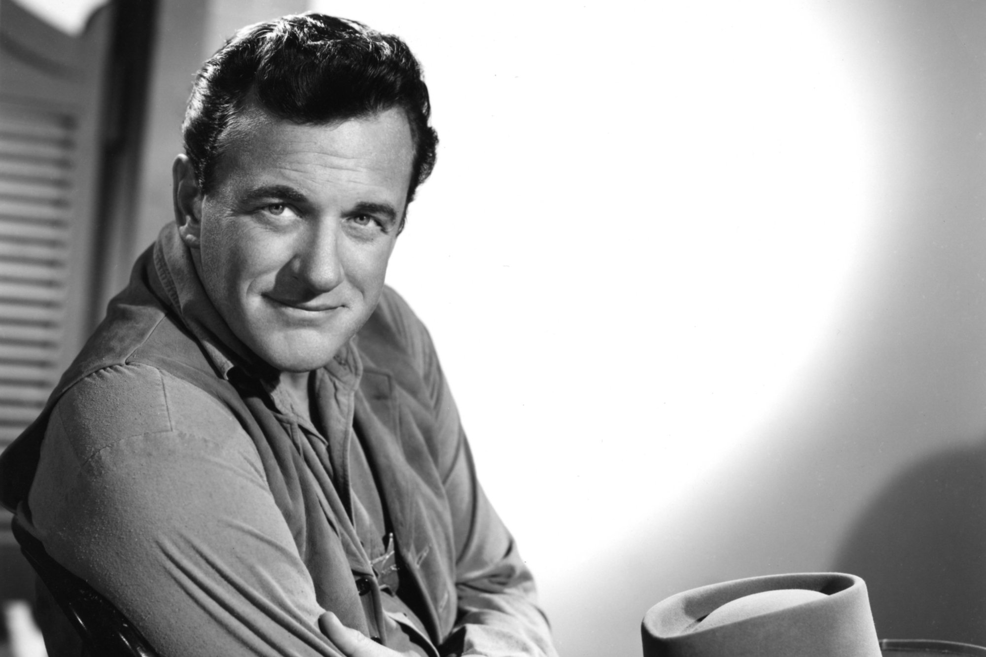 'Gunsmoke' actor James Arness posing in black-and-white picture wearing his Western costume with a cowboy hat resting in his lap