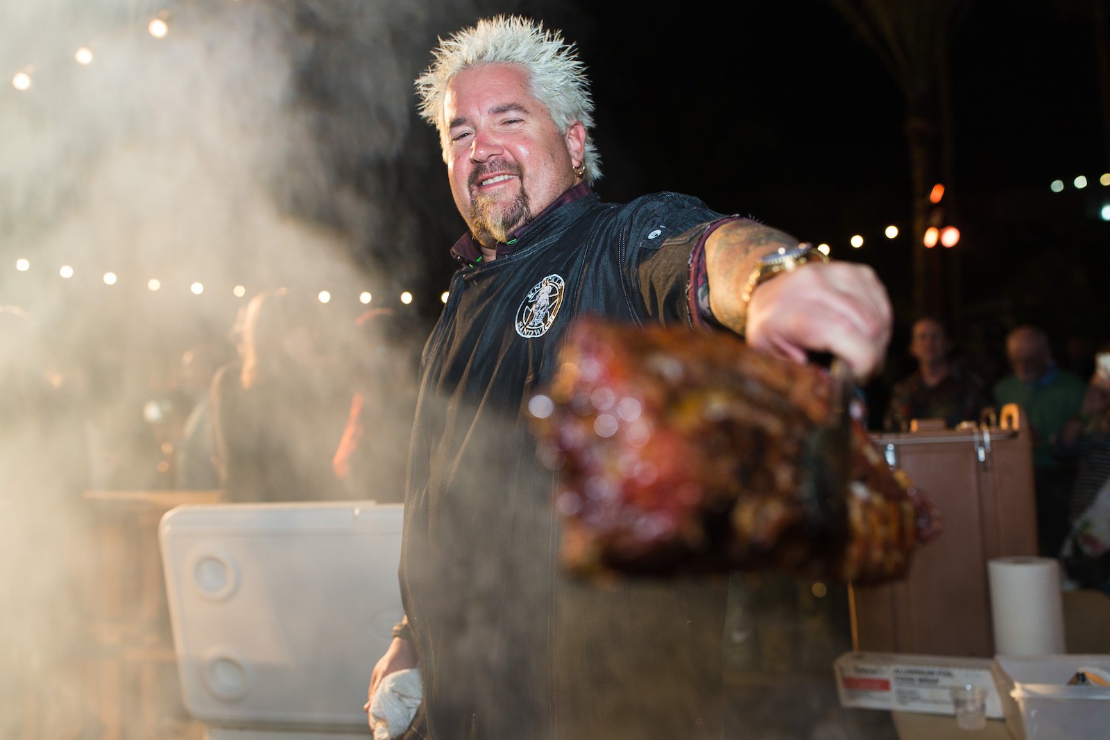 Chef Guy Fieri show a big piece of meat he is grilling to the camera 