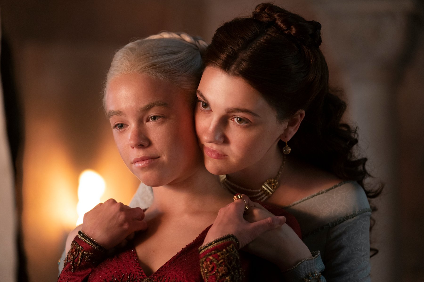 Milly Alcock and Emily Carey as Rhaenyra Targaryen and Alicent Hightower in an episode of 'House of the Dragon' Season 1. Alicent is standing behind Rhaenyra and their faces are touching.