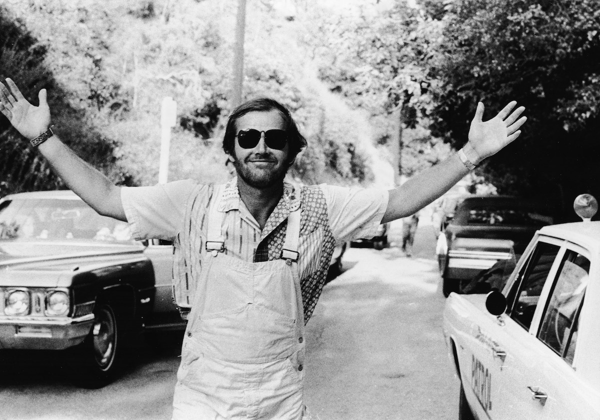 Actor Jack Nicholson smiles with his arms outstretched, wearing overalls and sunglasses, in 1972