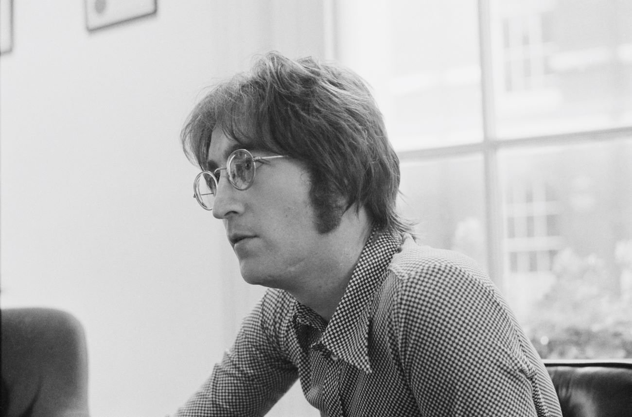 チェックのシャツと眼鏡をかけたジョン・レノンの白黒写真。