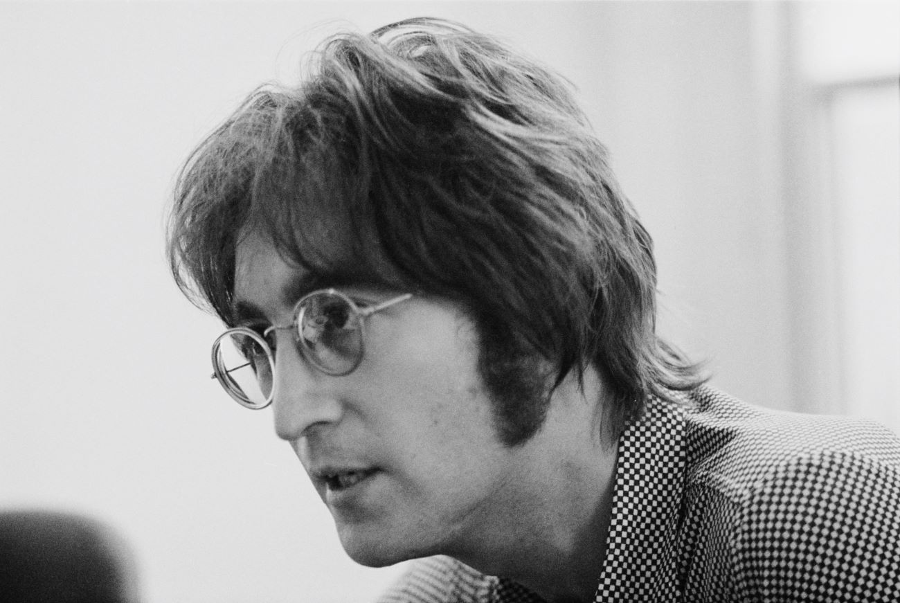 A black and white photo of John Lennon wearing a checkered shirt and glasses.