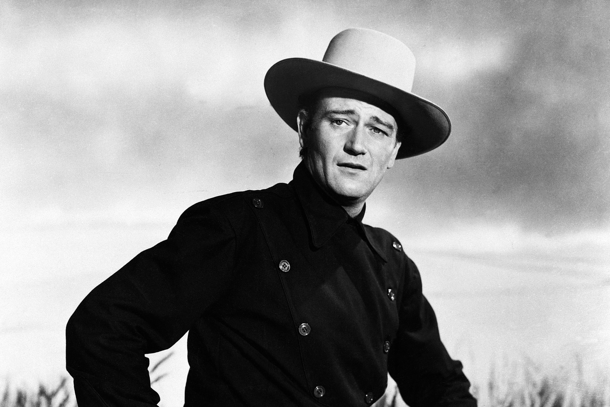 John Wayne, star of Western movies. He's wearing Western costume attire in a black-and-white photo.