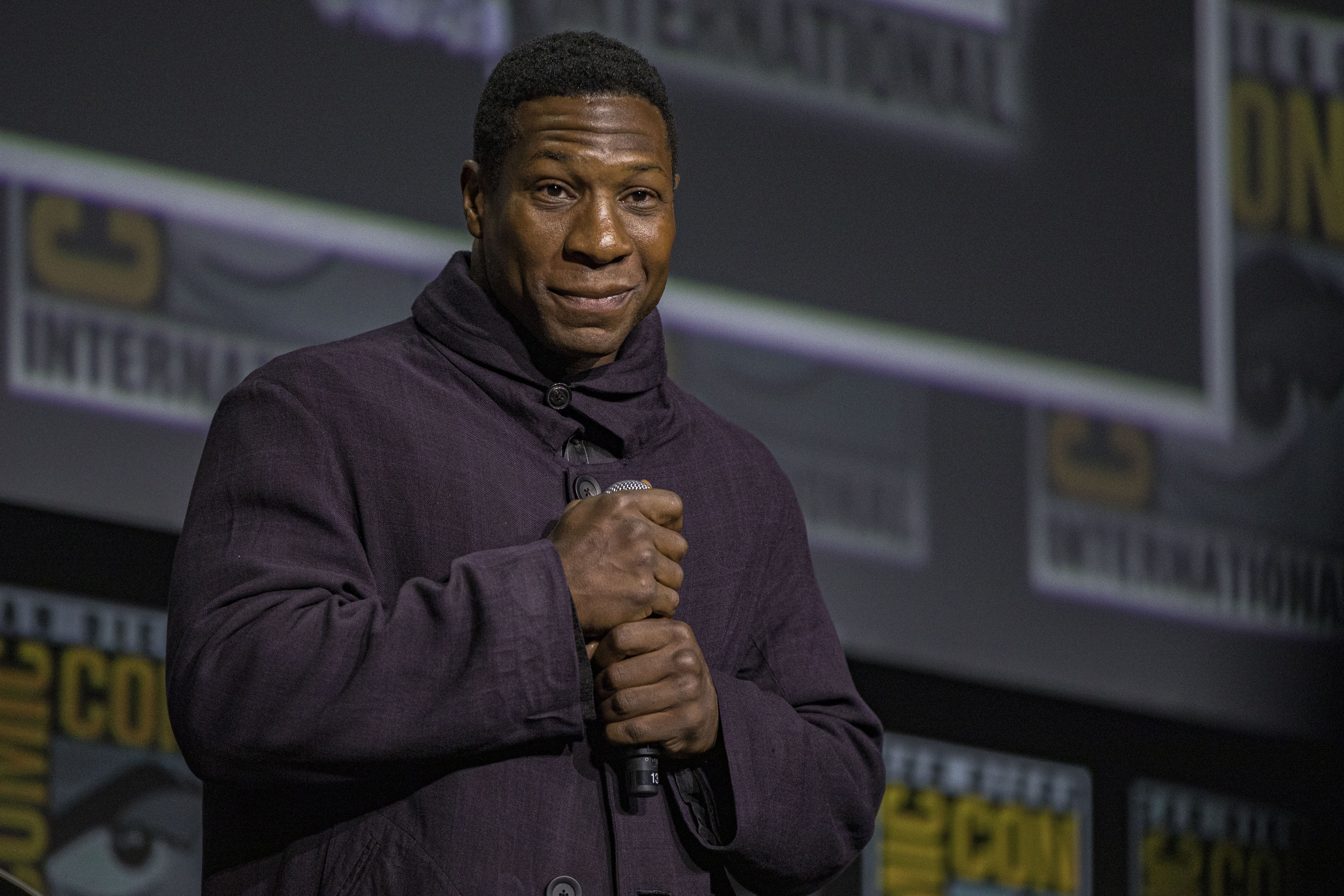 Jonathan Majors, who plays Kang the Conqueror in the MCU, wears a dark purple jacket while speaking onstage at San Diego Comic-Con 2022.