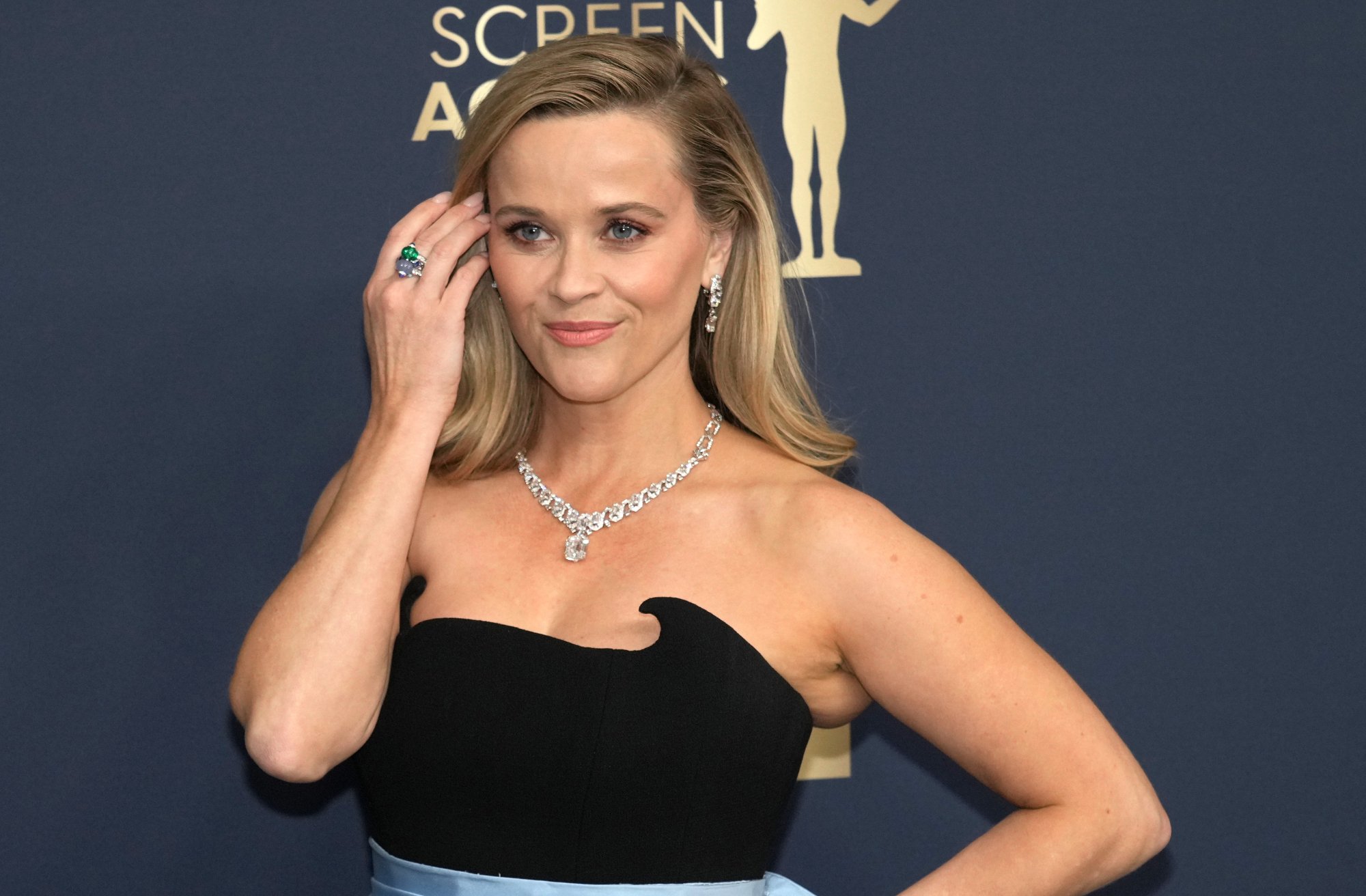'Legally Blonde 3' actor Reese Witherspoon wearing a black dress in front of Screen Actors Guild logo with her hand brushing back her hair behind her ear