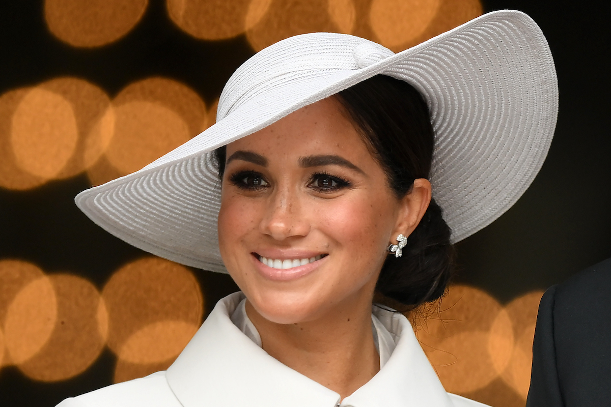 Meghan Markle, who said movies such as 'The Prince & Me' would've helped prepare her for royal life in an August 2022 The Cut interview, smiles wearing a white hat and coat