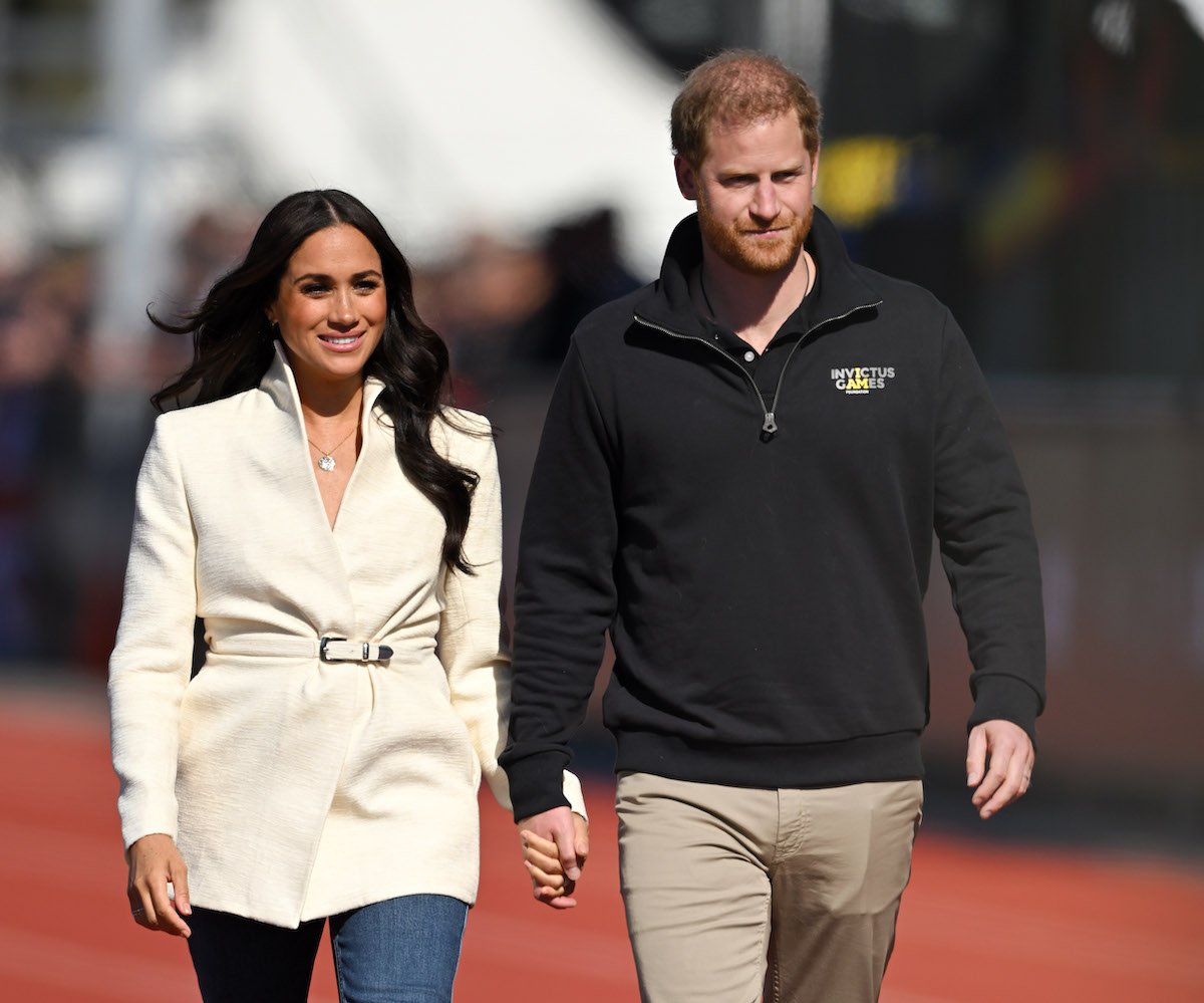 Meghan Markle and Prince Harry, who a royal author says will be 'acutely aware' of how 'strange' it will be if they don't visit the royal family during their September 2022 visit, walk hand-in-hand