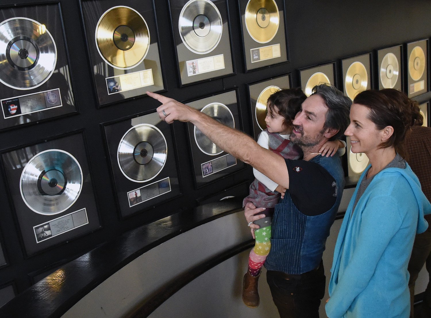 'American Pickers' star Mike Wolfe holding his daughter and pointing at a record on the wall with his wife, Jodi, next to him