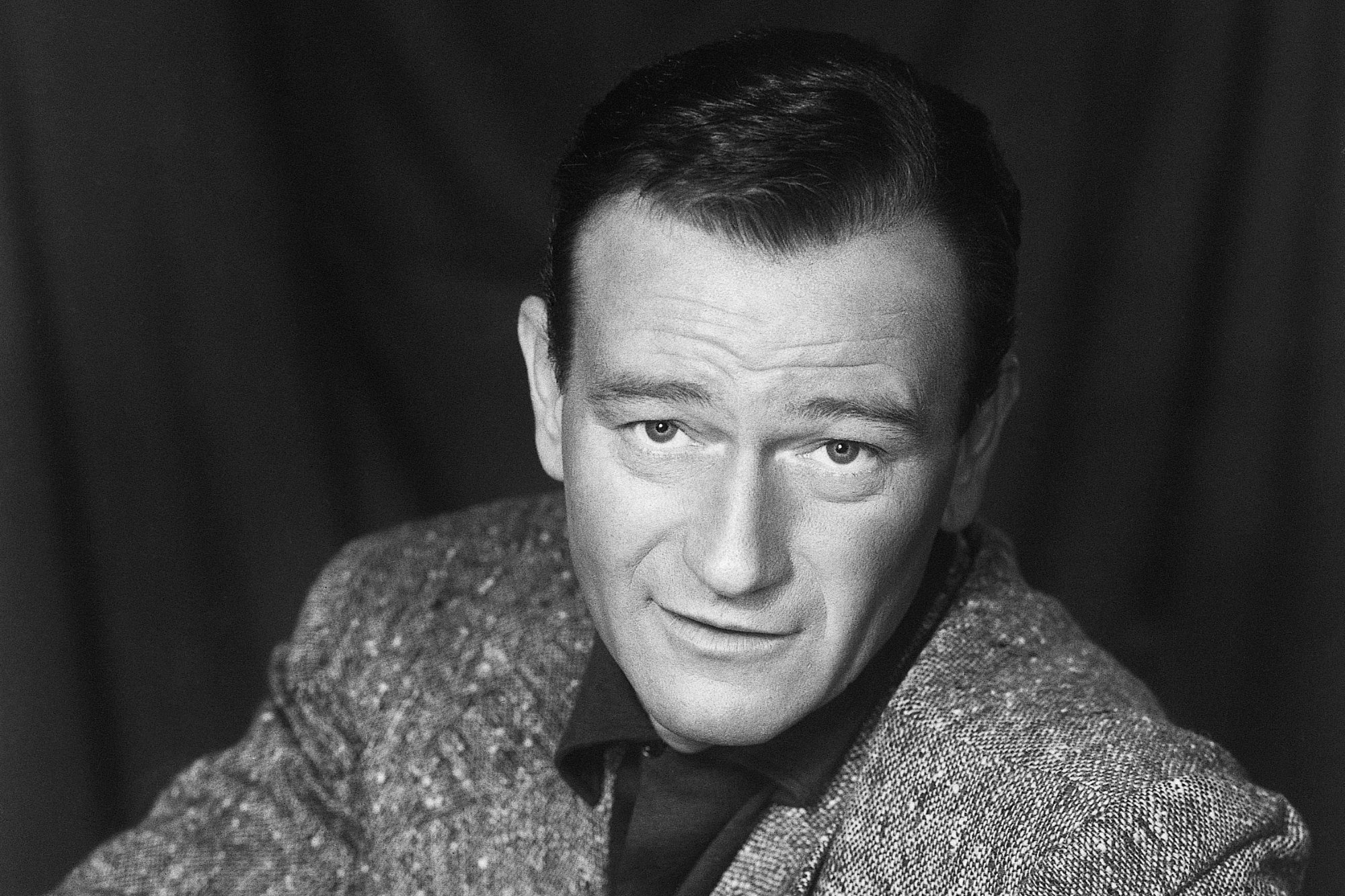 Movie star John Wayne seated, facing the back of the couch on which he is seated