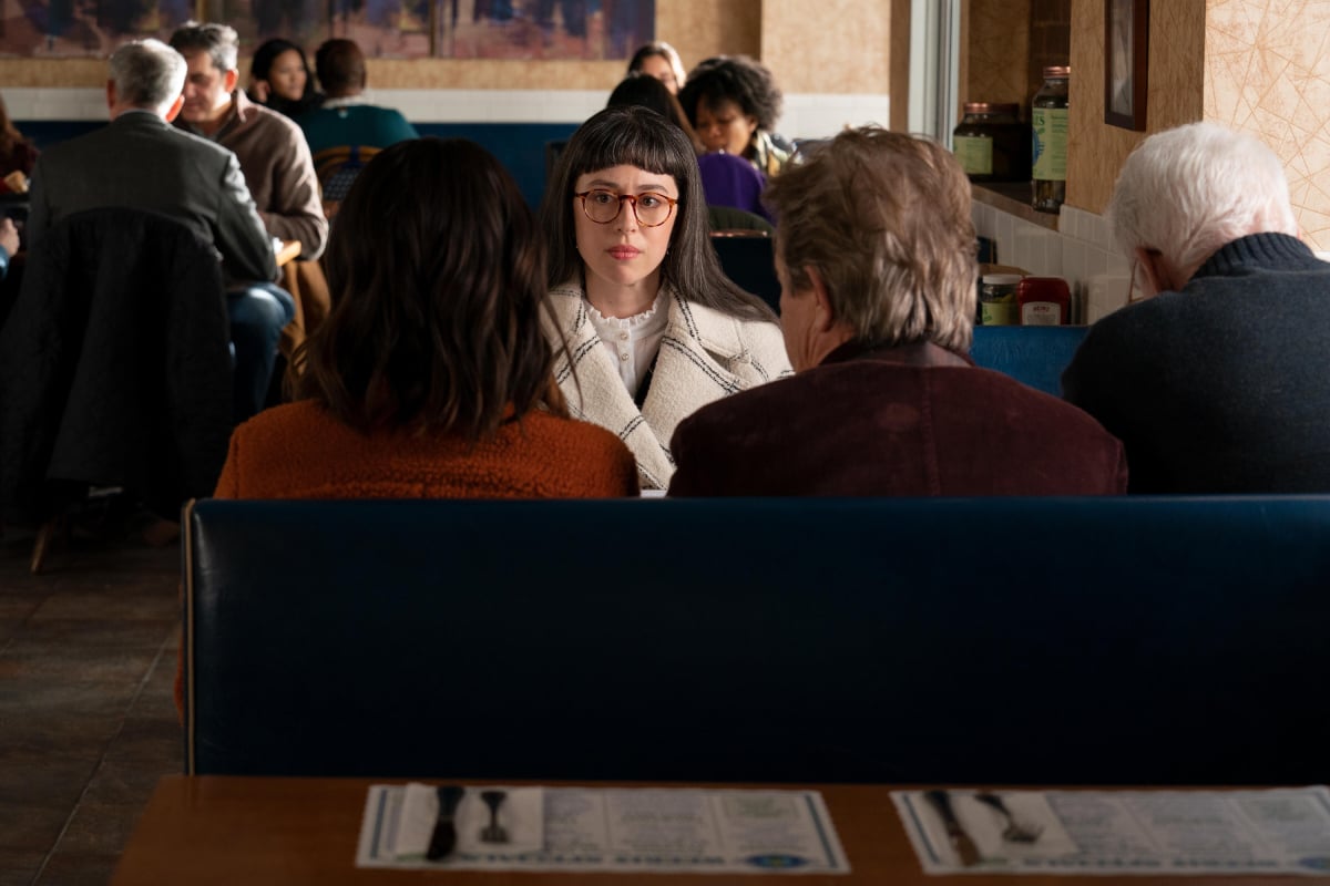 Adina Verson as Poppy White in Only Murders in the Building Season 2. Poppy sits across from Charles, Oliver, and Mabel at the Pickle Diner.