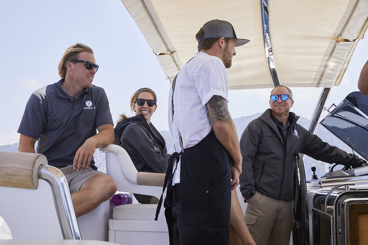 Paget Berry is seated next to Jenna MacGillivray, who is also seated. Adam Glick speaks to Captain Glenn Shephard on the Below Deck Sailing Yacht