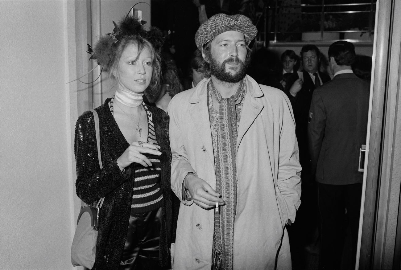 A black and white picture of Pattie Boyd and Eric Clapton holding cigarettes and standing in a doorway.