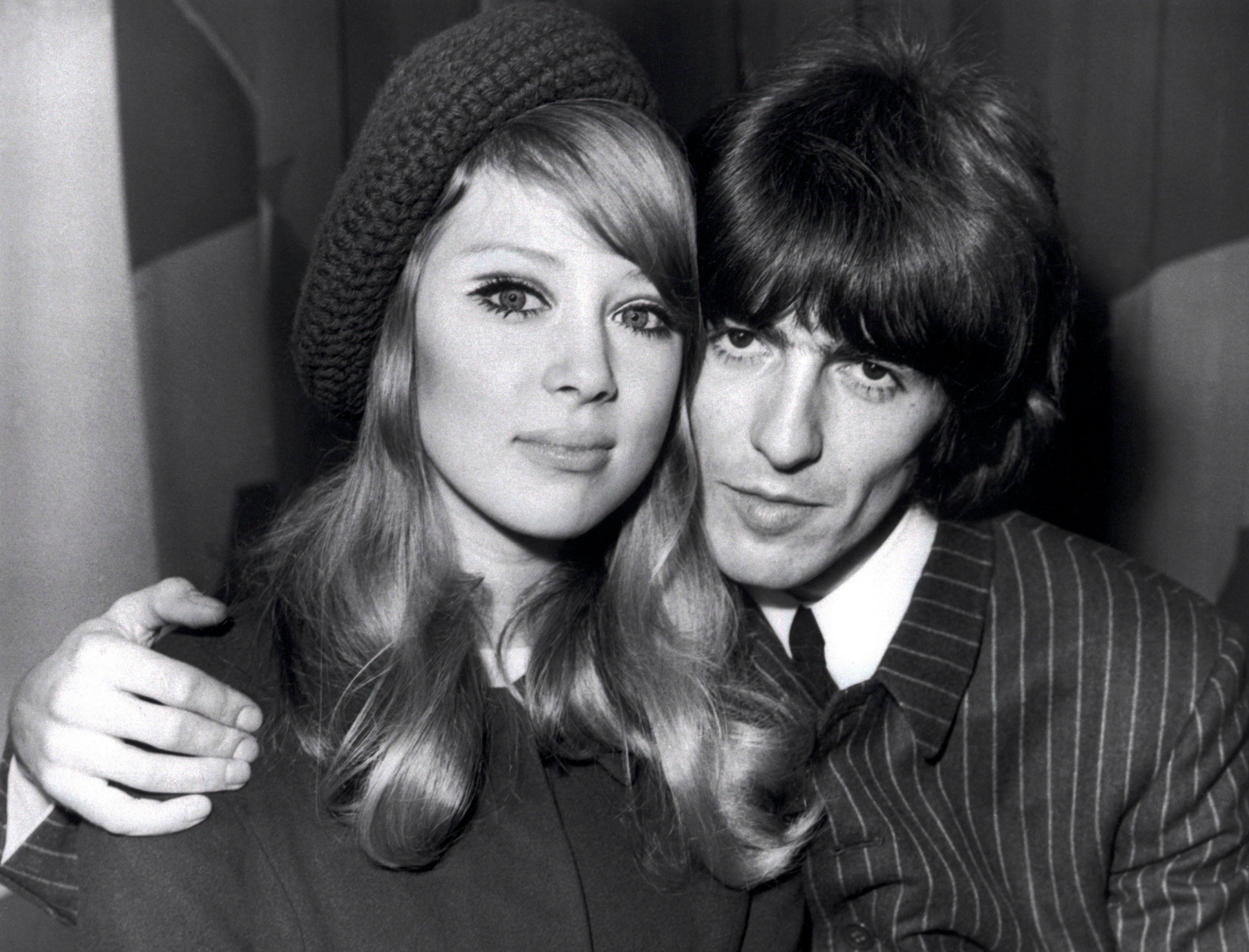 A black and white picture of George Harrison sitting with his arm around Pattie Boyd. 