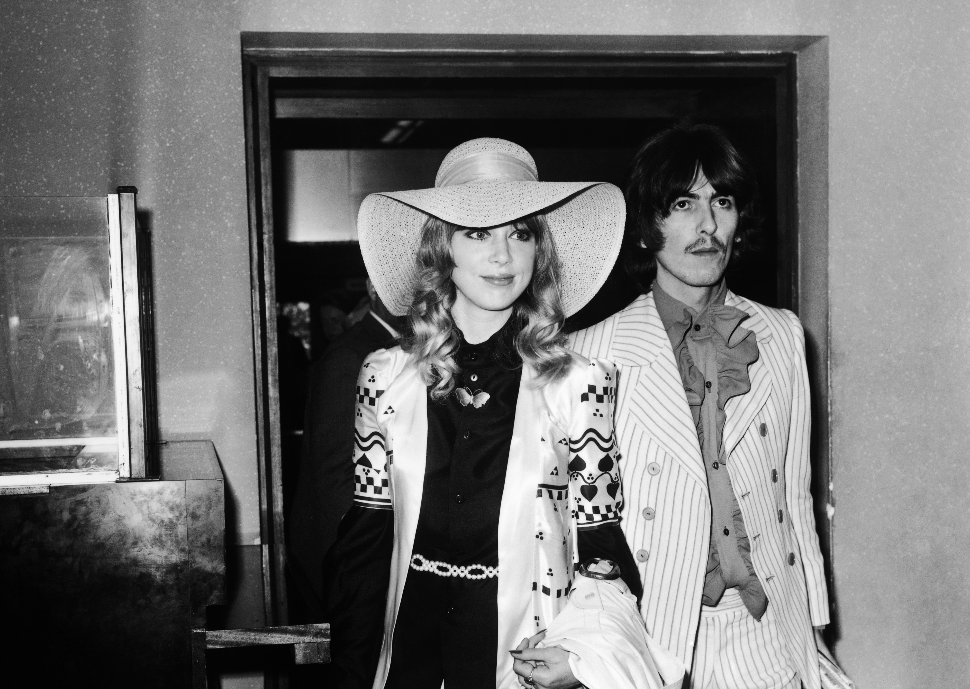 A black and white picture of Pattie Boyd and George Harrison walking through a doorway.