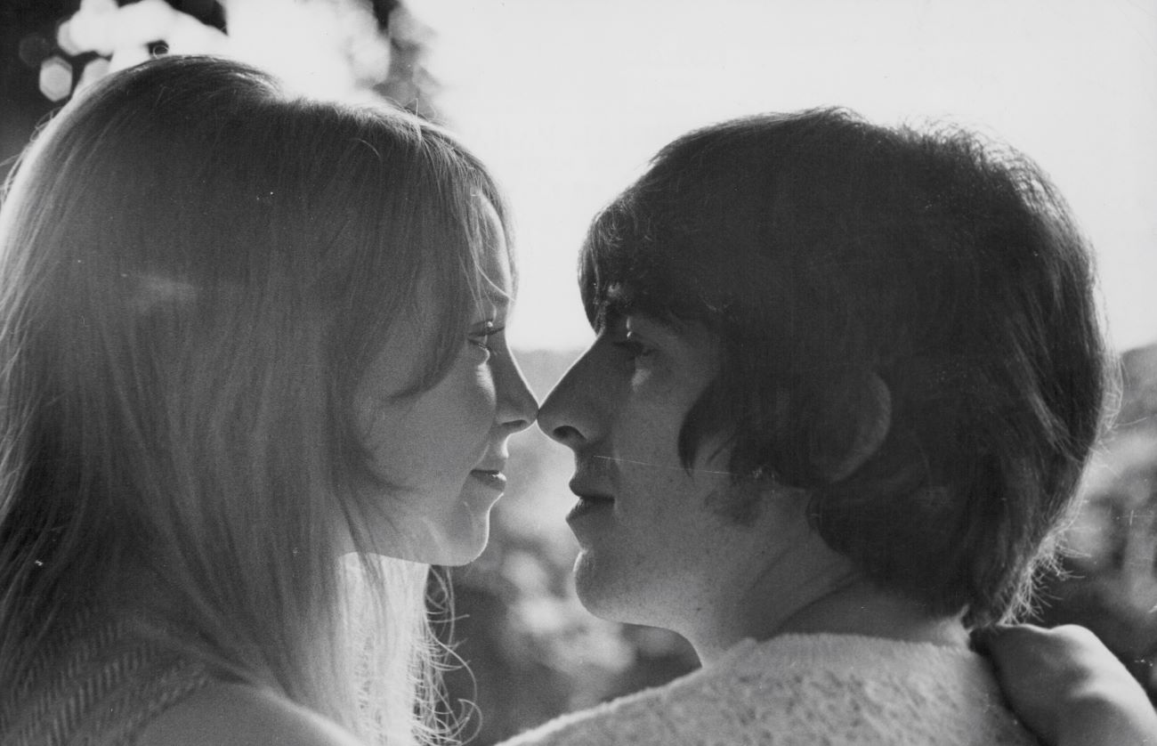 A black and white picture of Pattie Boyd and George Harrison sitting with their noses touching. 