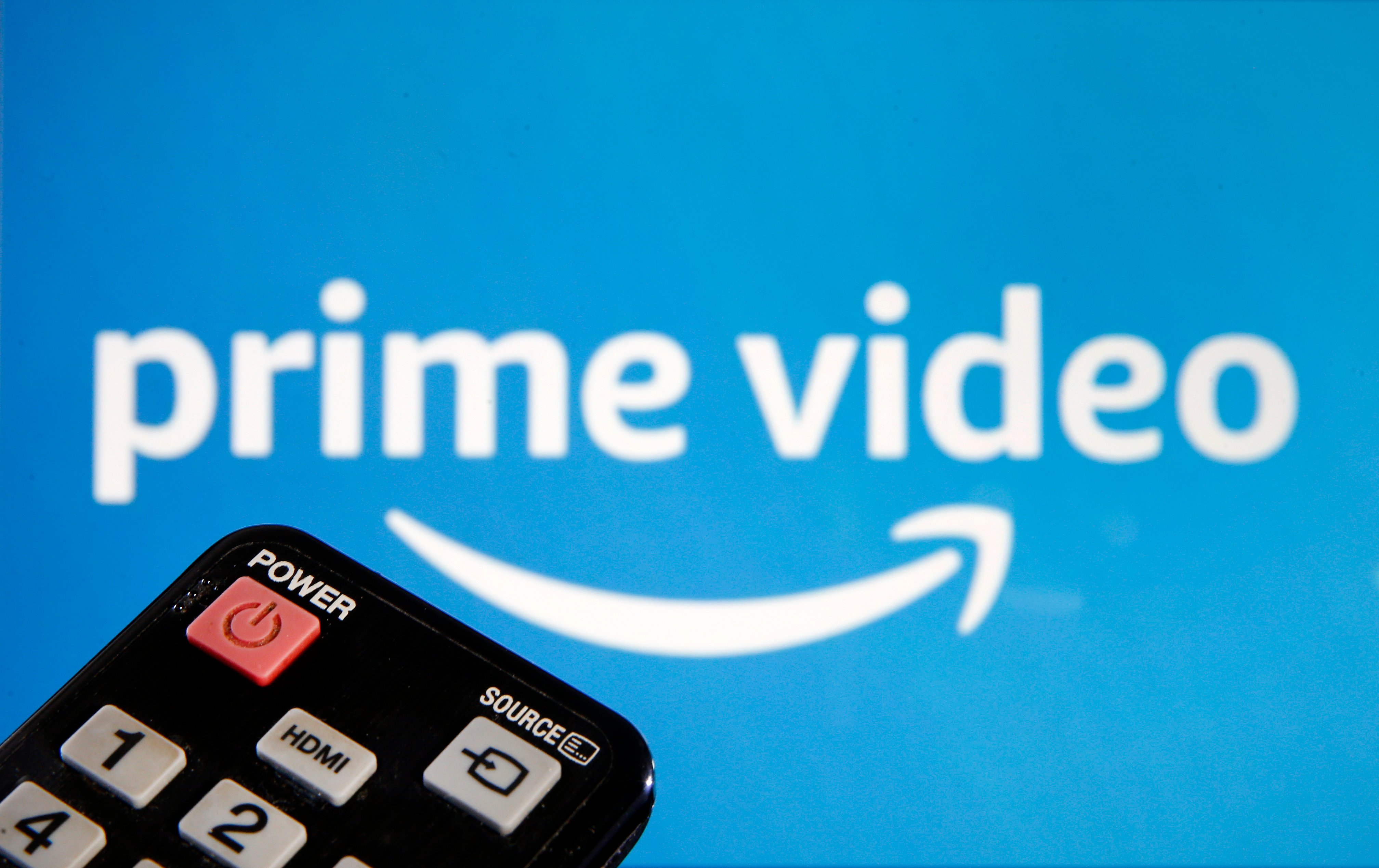 a remote control is seen in front of a television screen showing a Prime Video logo