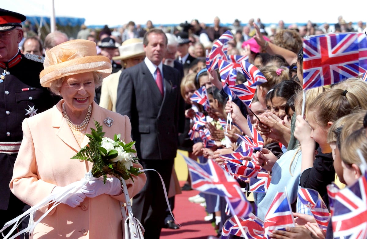 Queen Elizabeth, who is one of the royal family members with nicknames, smiles holding flowers as she greets crowds