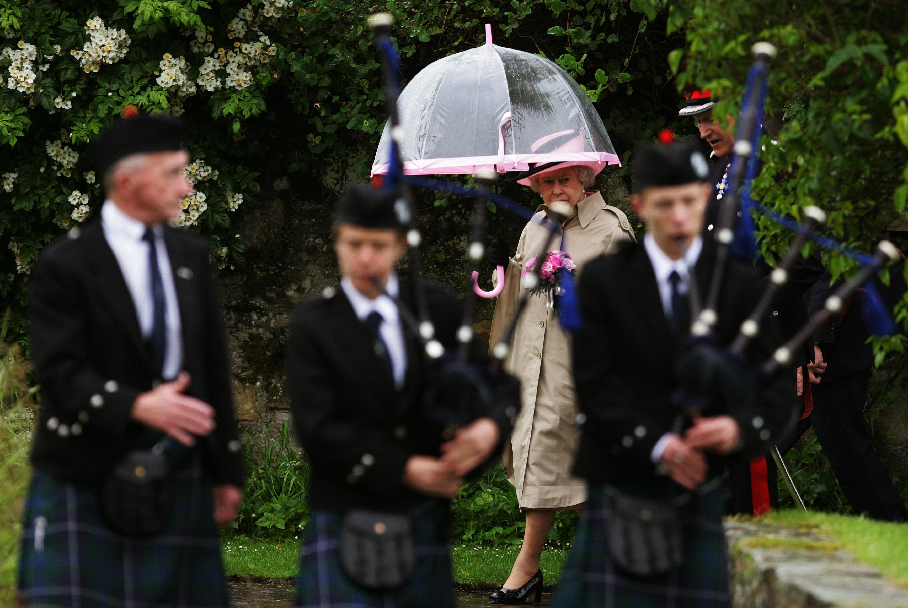 Queen Elizabeth II watching men play bagpipes in the rain