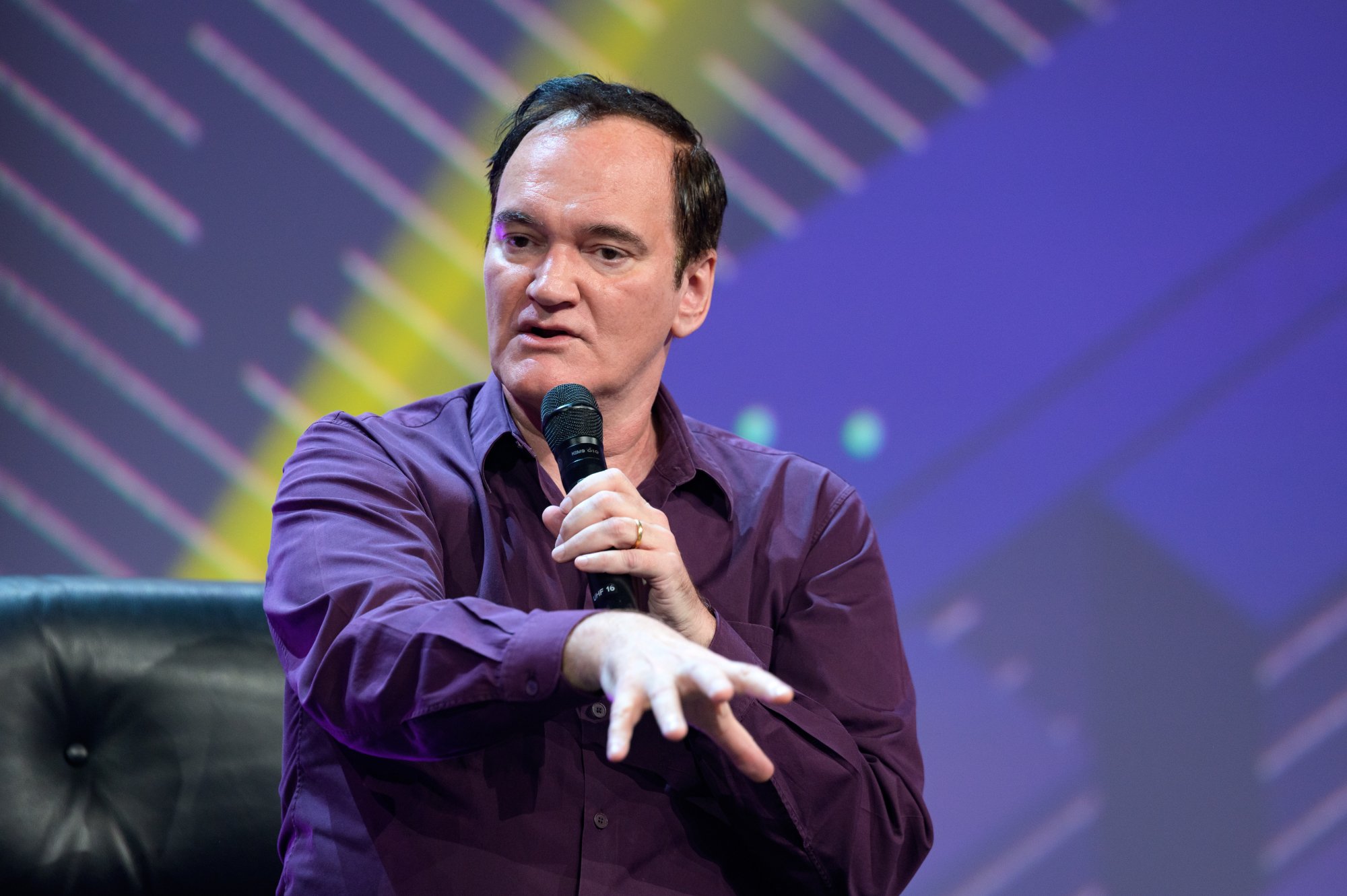 Quentin Tarantino, who loved 'Top Gun: Maverick'. He's wearing a purple collared shirt and talking into a microphone.
